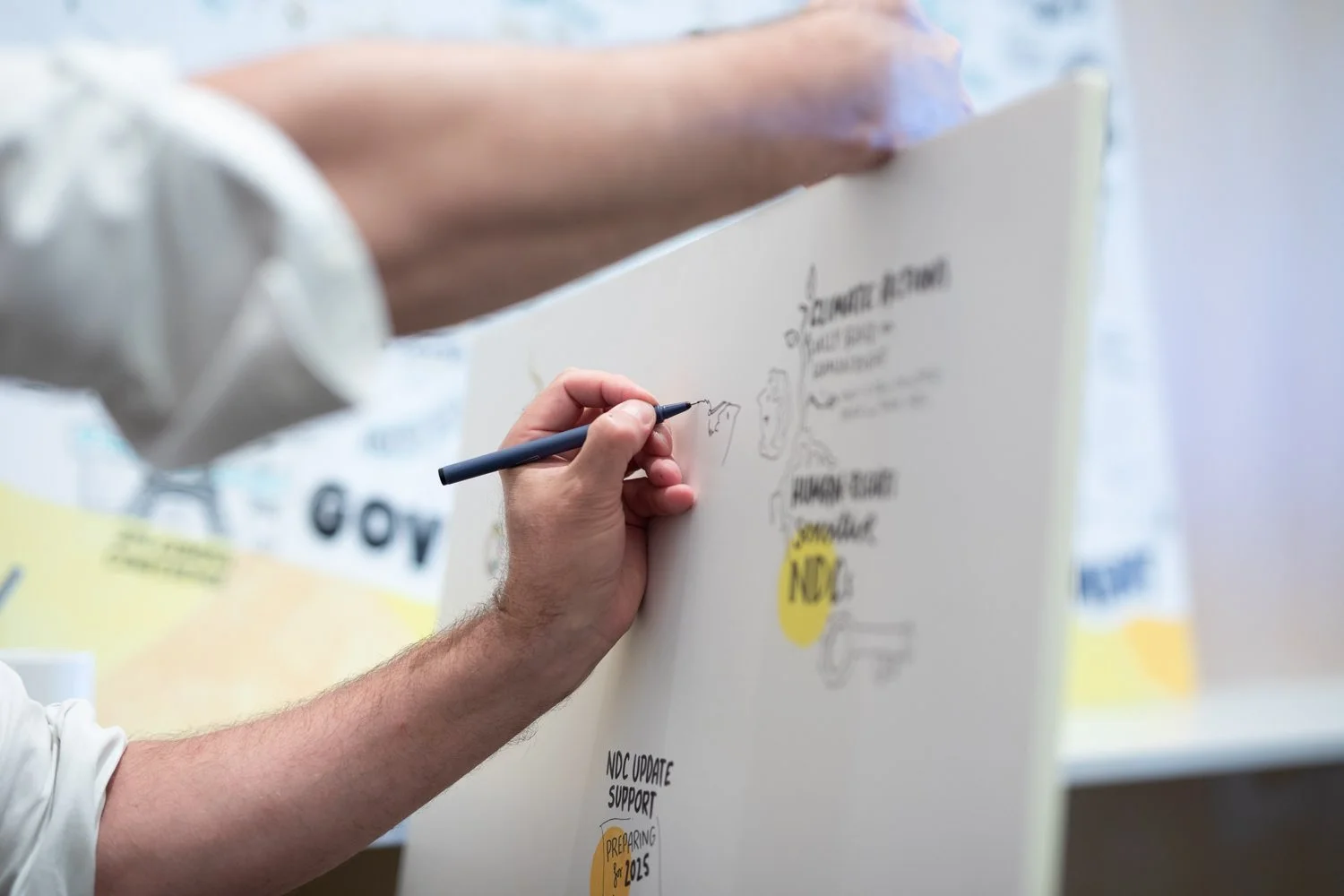 Ein Mensch zeichnet auf eine große weiße Tafel, es sind handschriftliche Notizen und Grafiken sichtbar.