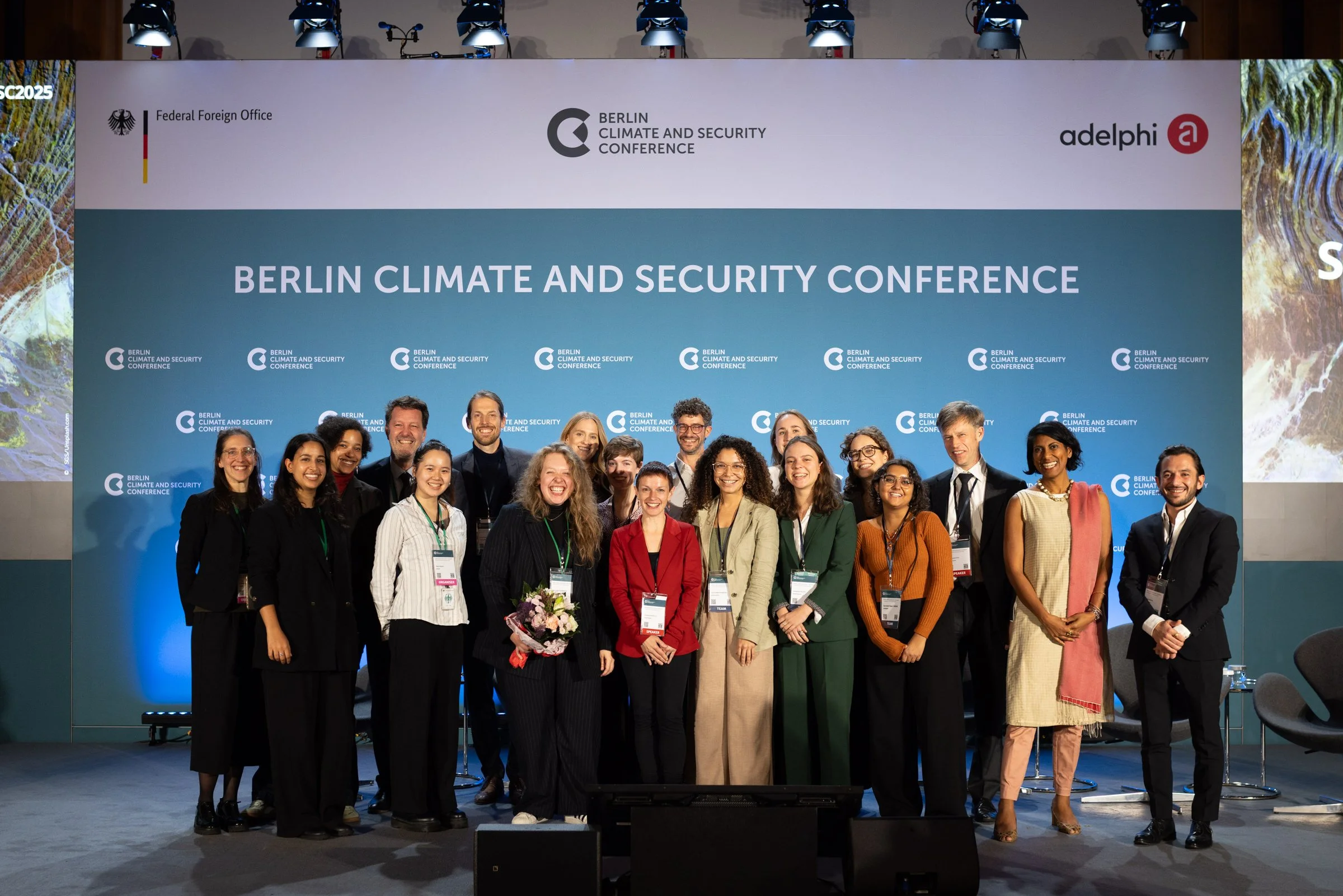Gruppenfoto mit mehreren Frauen und Männern, die an der Berliner Klima- und Sicherheitskonferenz teilnehmen, vor einem großen Banner mit den Logos der Veranstaltung.