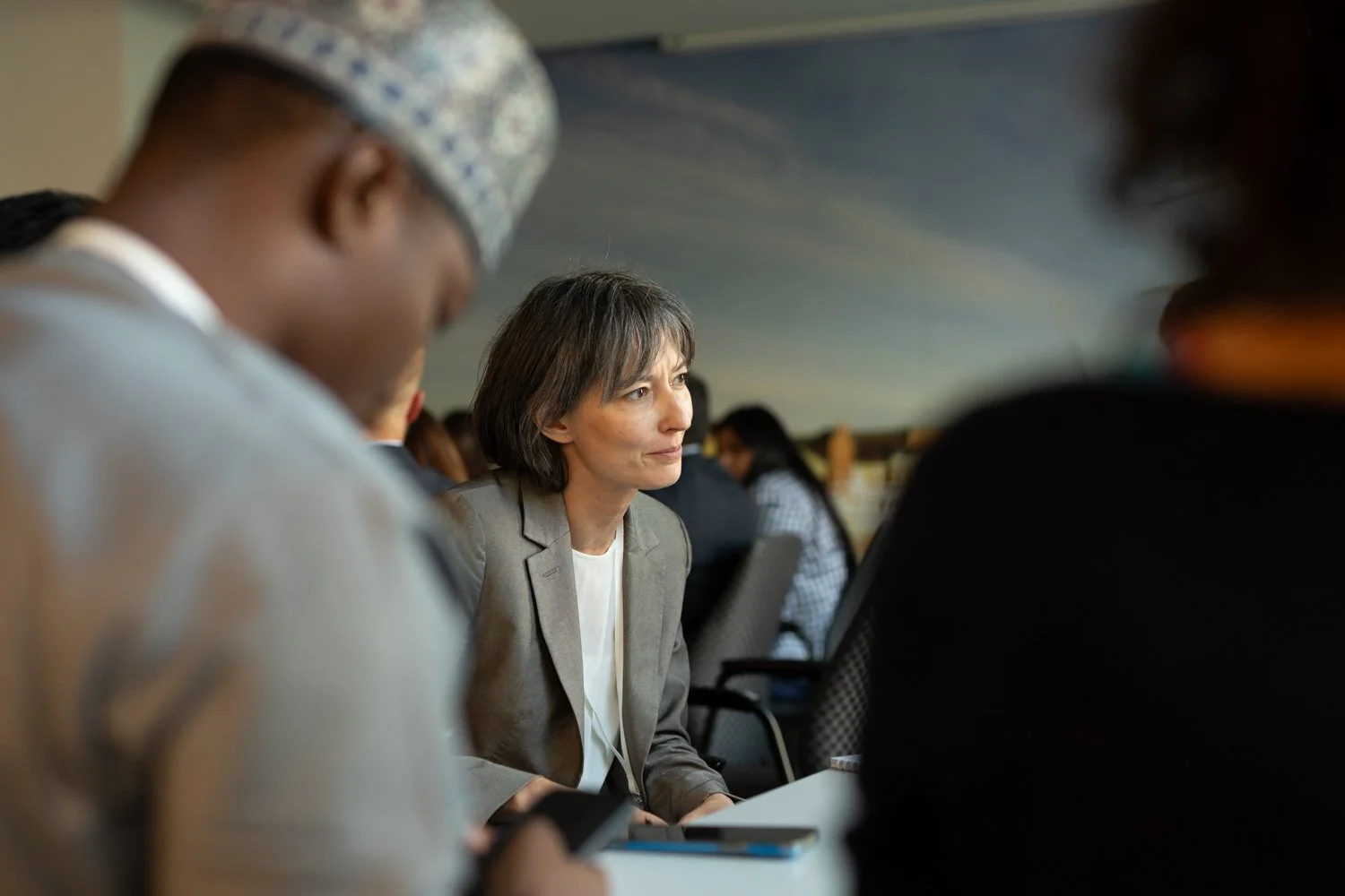 Eine Frau in einem grauen Blazer sitzt in einem Konferenzraum und hört aufmerksam zu.