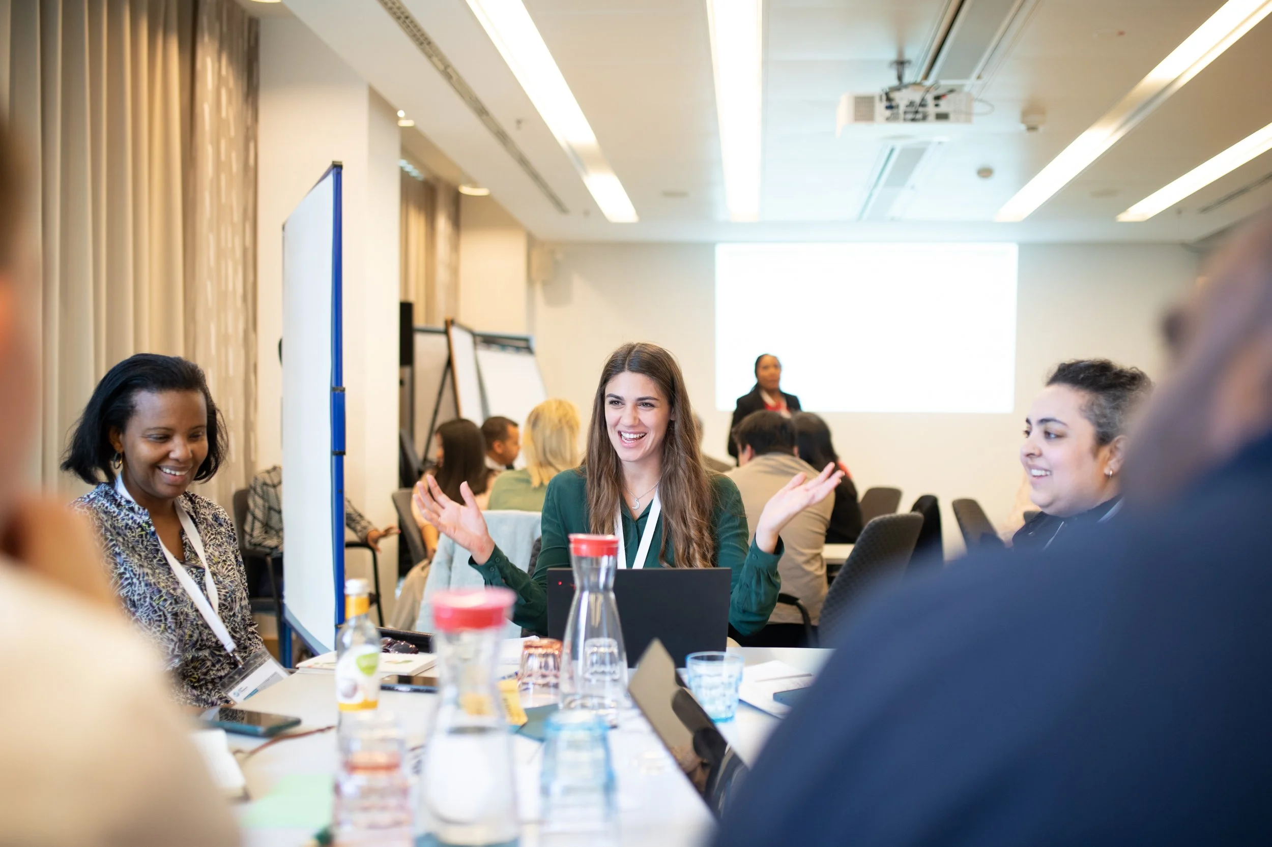Menschen nehmen an einer Konferenz oder einem Workshop in einem großen Tagungsraum teil, mit einem Vortrag im Hintergrund auf einer großen Leinwand.