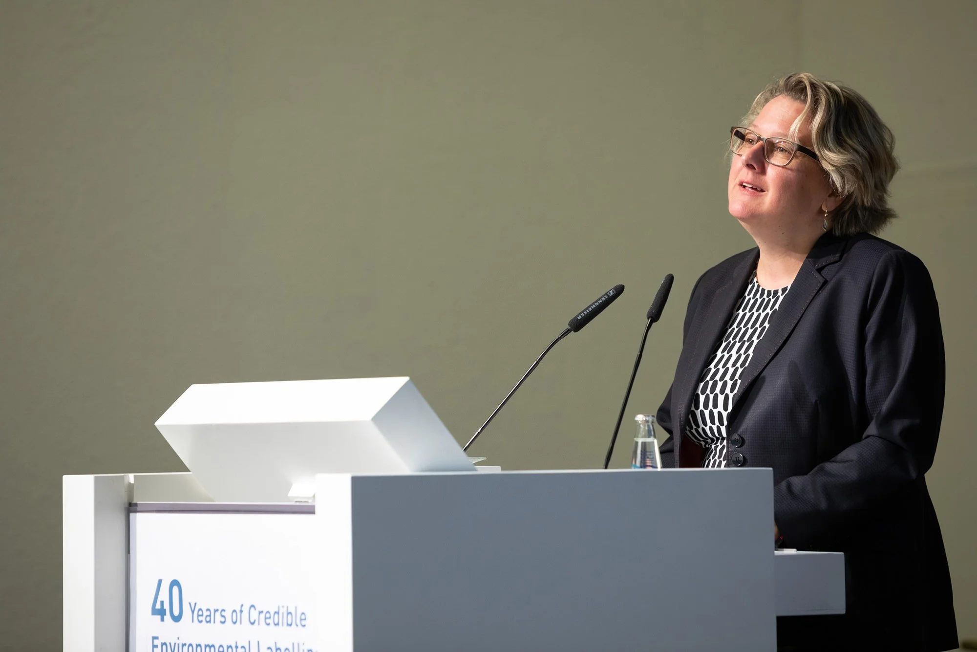 Umweltministerin Svenja Schulze steht an einem Rednerpult bei einer Präsentation, trägt eine schwarze Brille und ein schwarzes Jackett, im Hintergrund eine graue Wand.