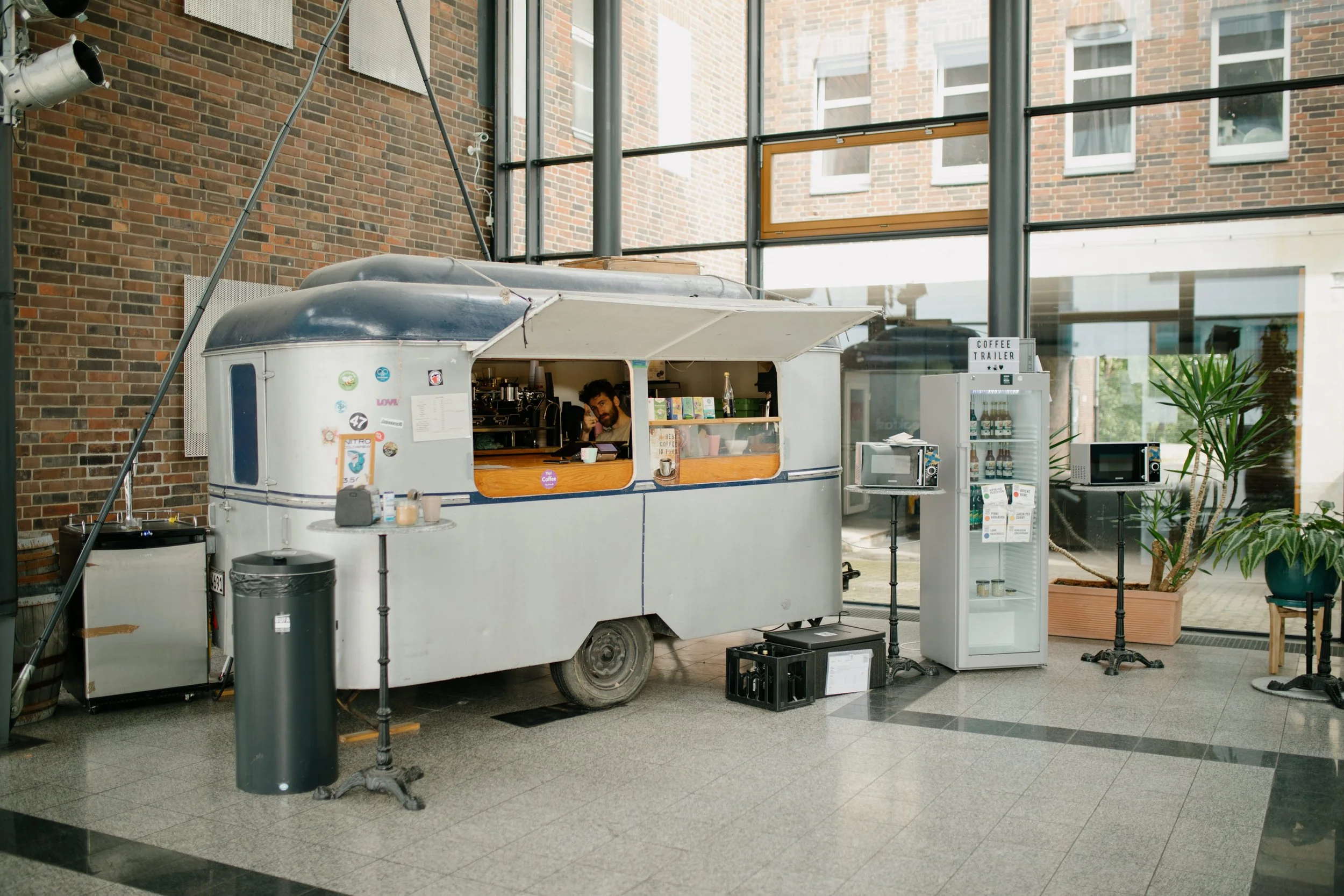 Ein Food-Truck in einem Innenraum, mit einer Person, die drin sitzt, und einem Getränkeautomat daneben.