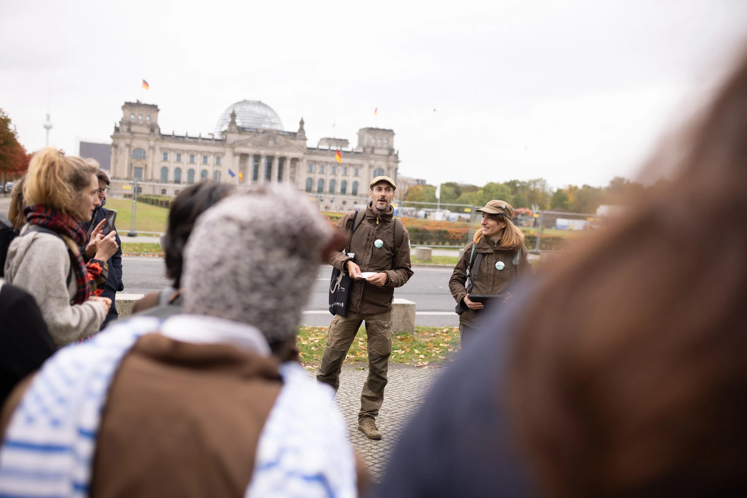 Gruppen von Touristen unterhalten sich vor dem Berliner Reichstagsgebäude, einige machen Fotos und hören einem Guide zu.