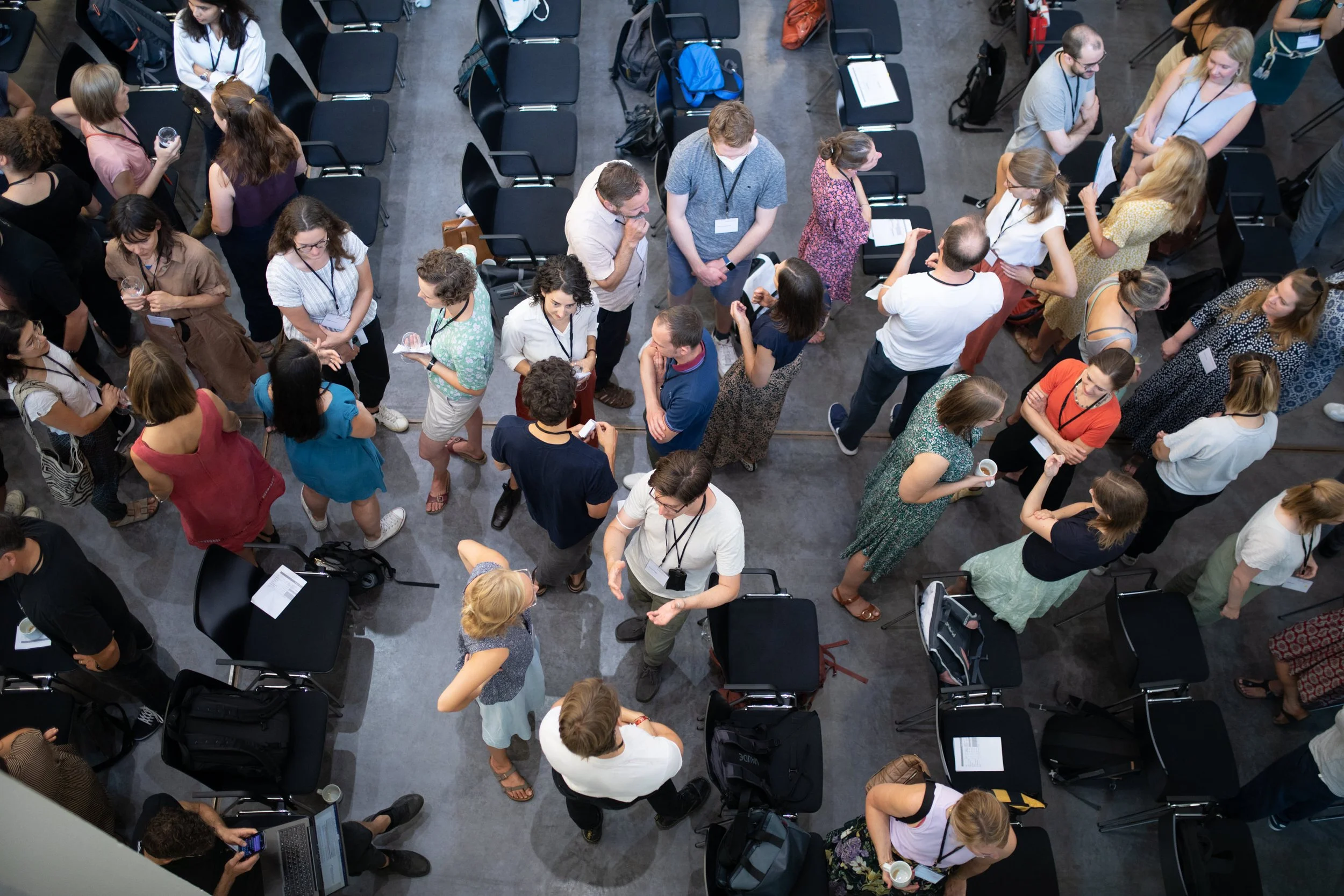 Vogelperspektive auf eine Gruppe von Menschen, die auf einer Konferenz oder einem Treffen in einem großen Raum miteinander sprechen, einige sitzen, andere stehen.