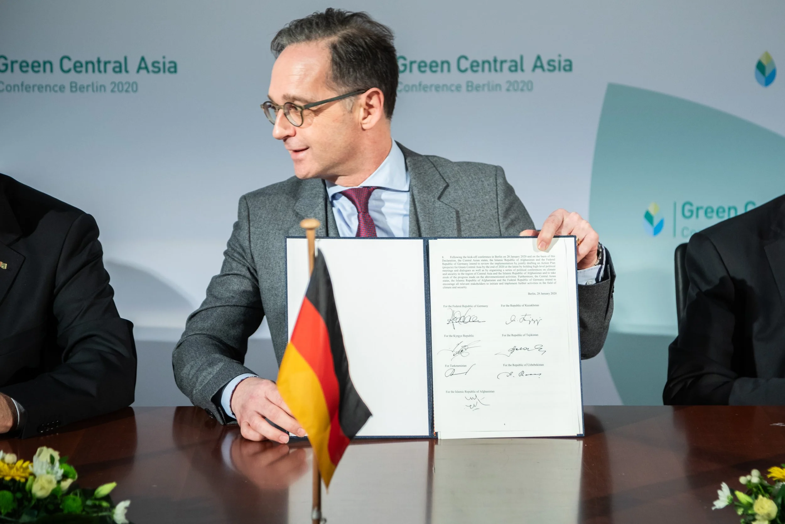 Außenminister Heiko Maas zeigt eine unterschriebene Urkunde, neben einem kleinen deutschen und einem turkmenischen Flaggen auf dem Tisch.