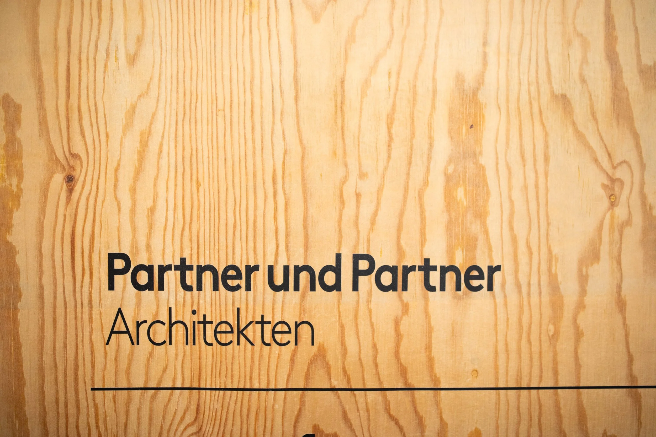 Holzoberfläche mit deutschen Texten über Partner und Architekten.