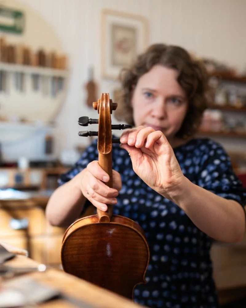 Frau überprüft eine Geige in einem Atelier.