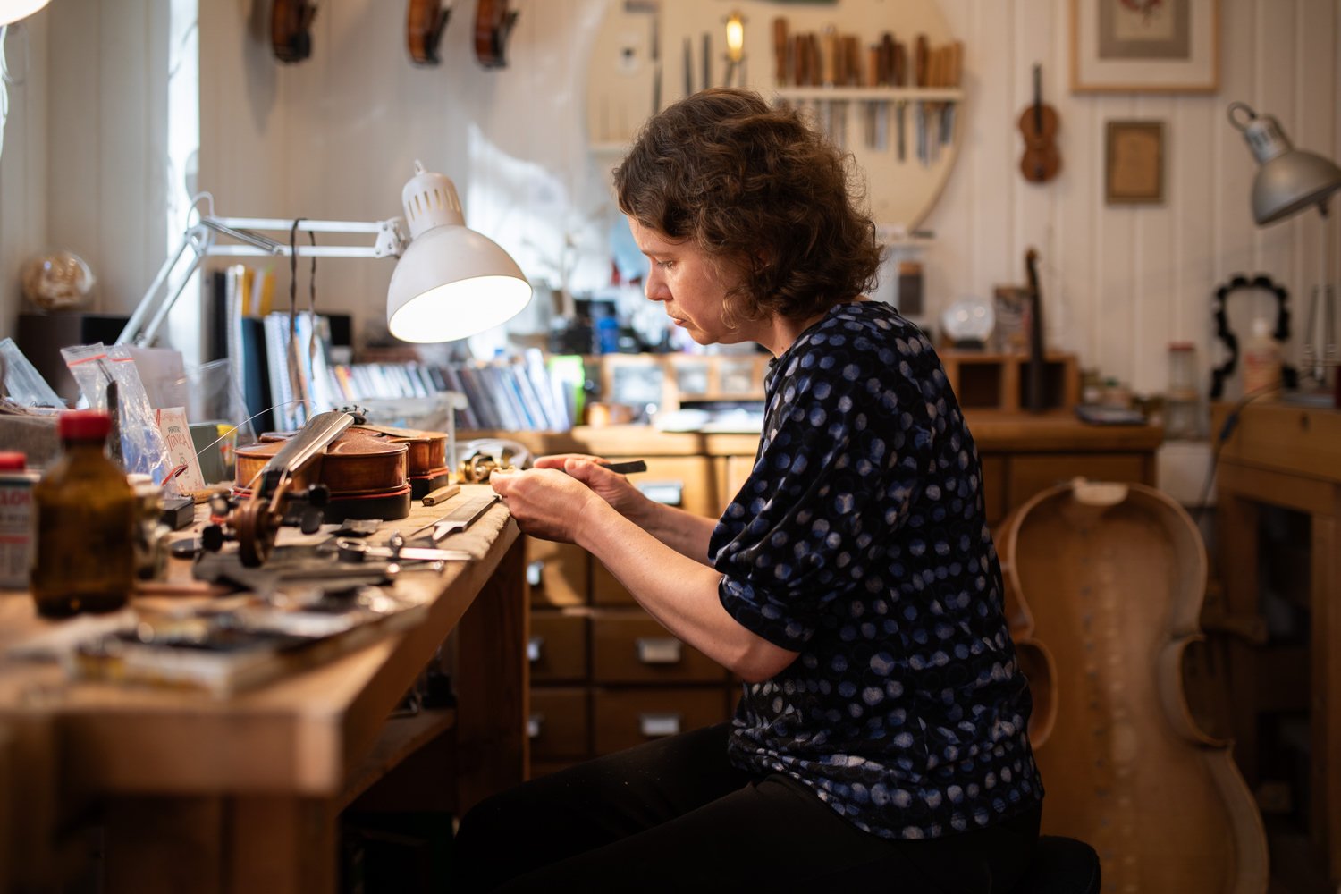 Frau arbeitet an einem Schreibtisch in einem Musikatelier, umgeben von Musikinstrumenten und Werkzeugen.