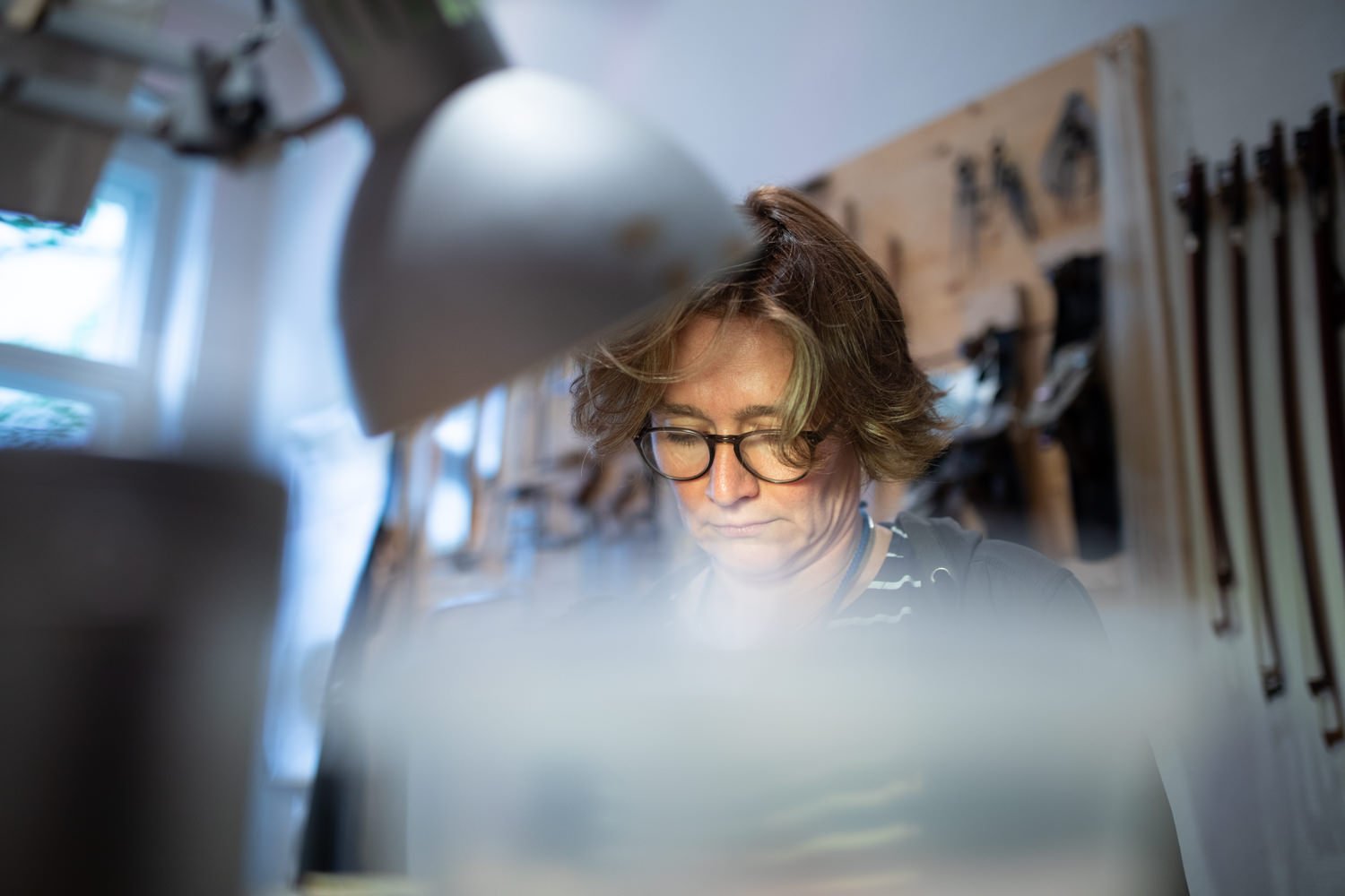 Ein Mädchen mit Brille arbeitet in einer Holzwerkstatt, die mit Werkzeugen an einer Wand ausgestattet ist.