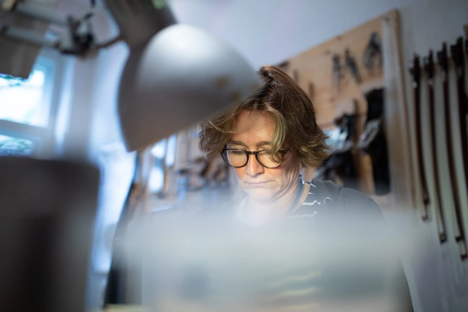 Ein Mädchen mit Brille arbeitet in einer Holzwerkstatt, die mit Werkzeugen an einer Wand ausgestattet ist.