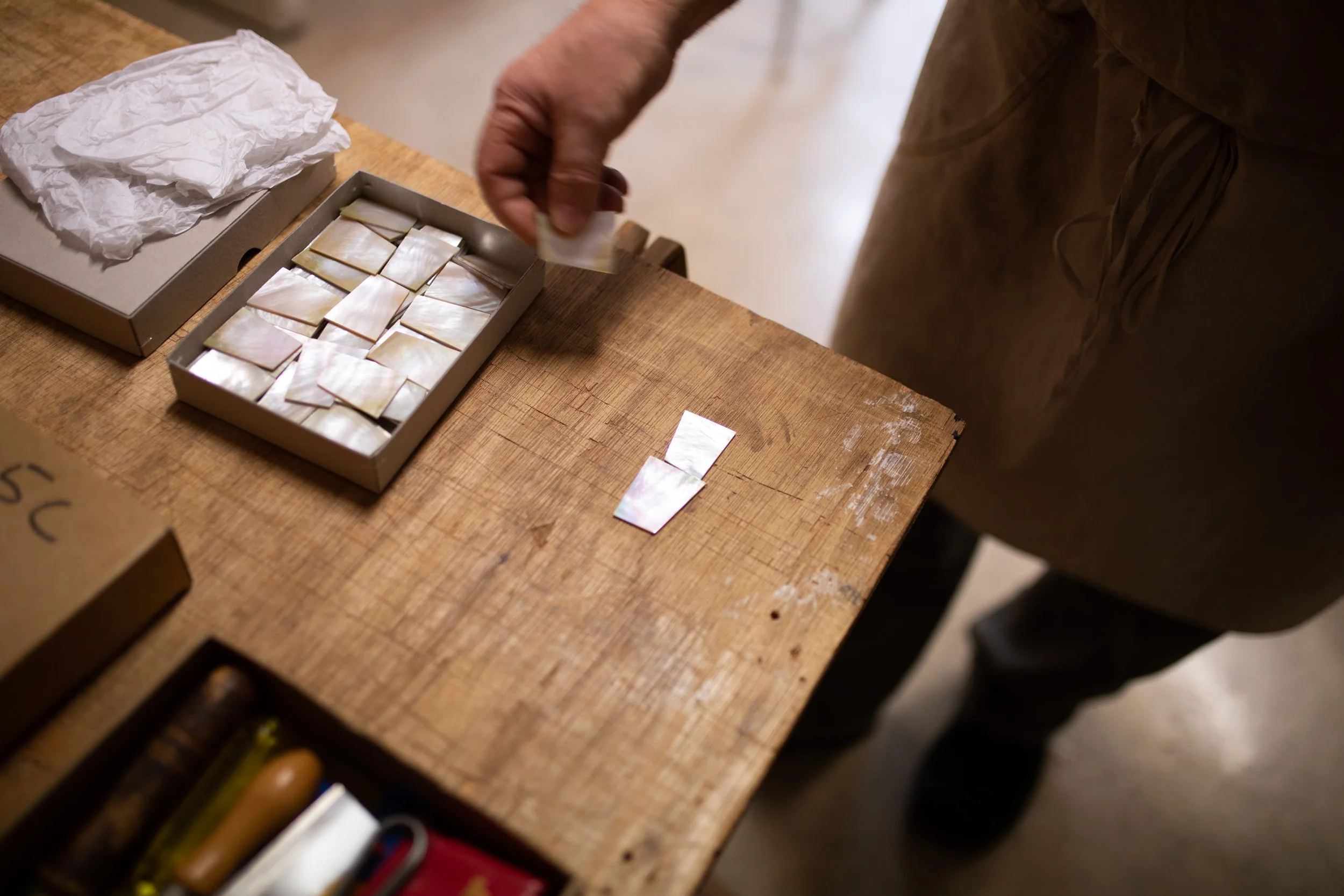 Hand legt kleine quadratische Gegenstände in eine Schachtel auf einem Holztisch, daneben liegt Packpapier.