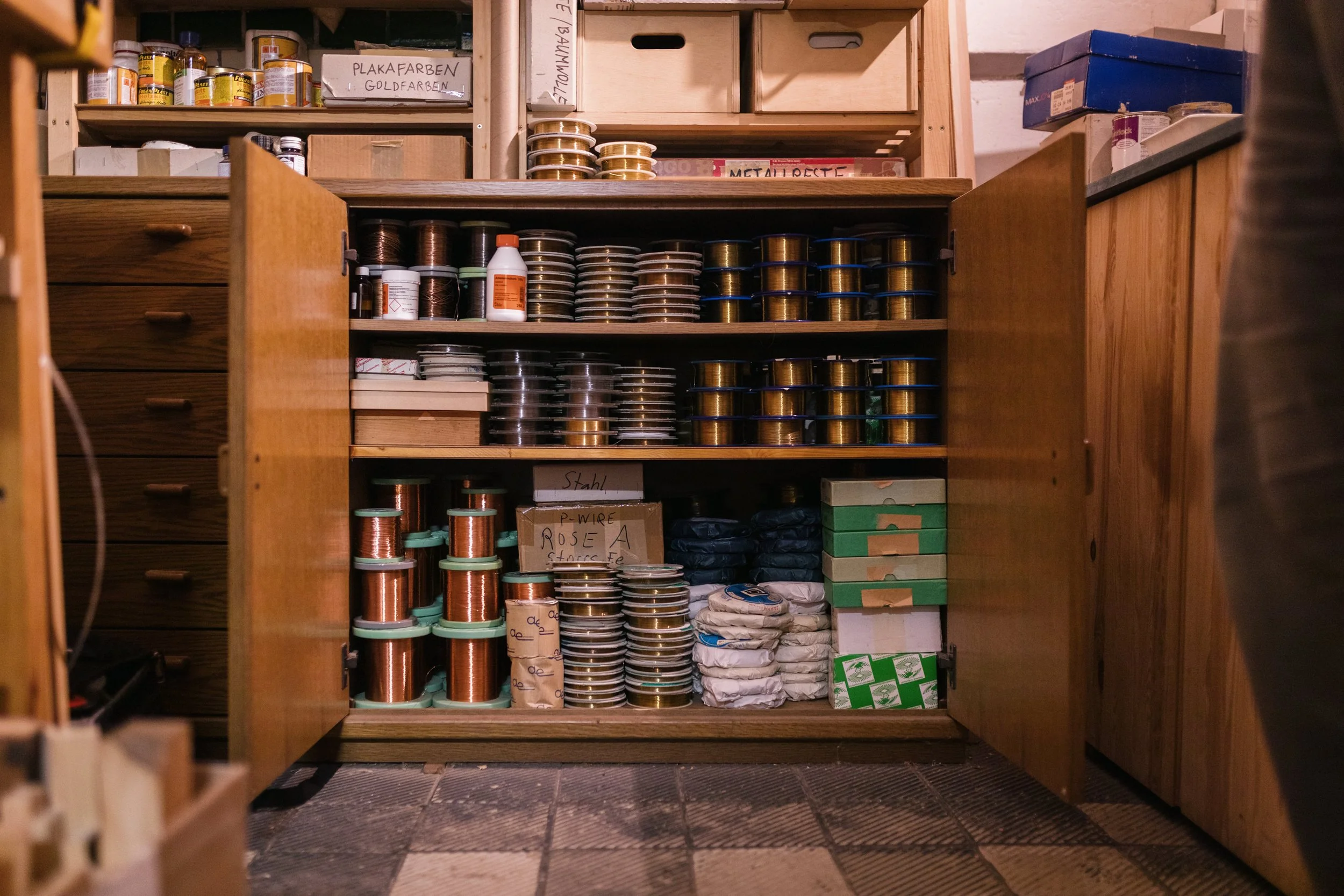 Holzschrank mit Spulen von Draht, Büchern und Papiertüten, in einem Werkraum oder Lagerraum.