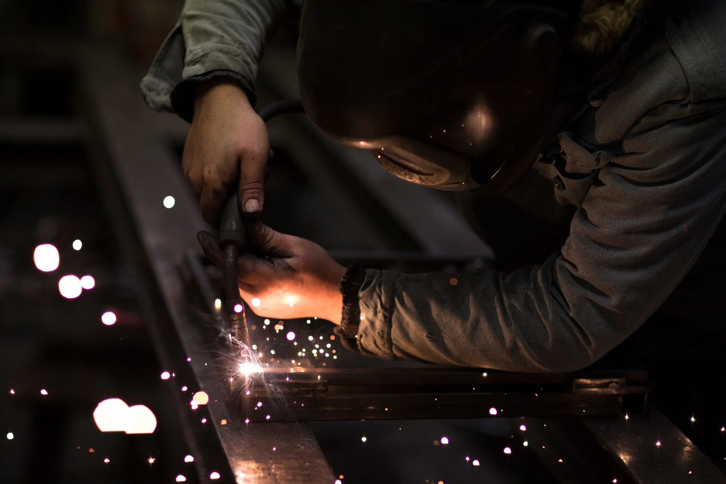 Ein Handwerker schweißt Metall, während Funken sprühen in einer dunklen Werkstatt.