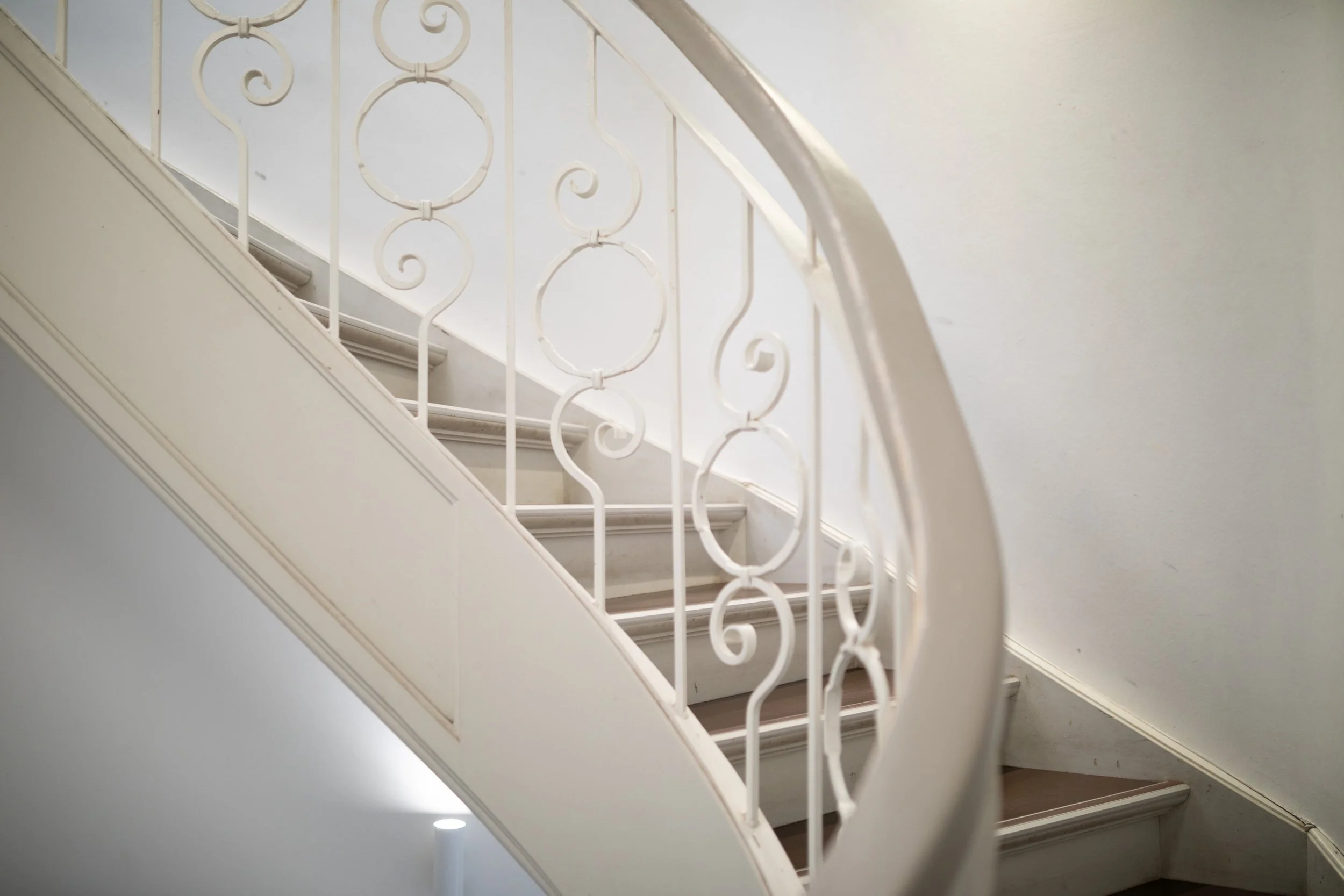 Innenaufnahme einer Treppe mit weißen Geländern und Holzstufen an einer weißen Wand.