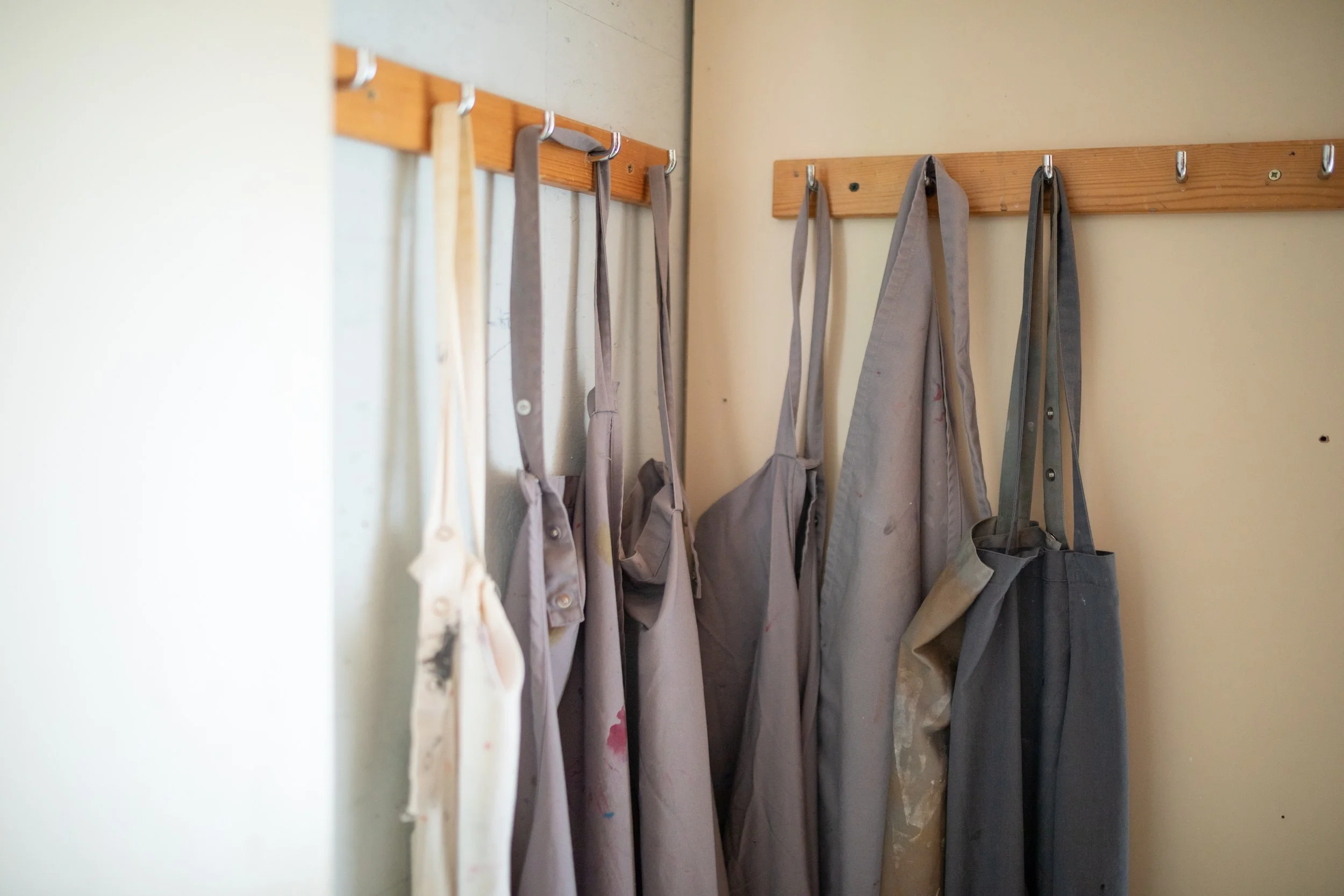Hakenleiste mit mehreren Stofftaschen und Kleidungsstücken, an einer gelben Wand