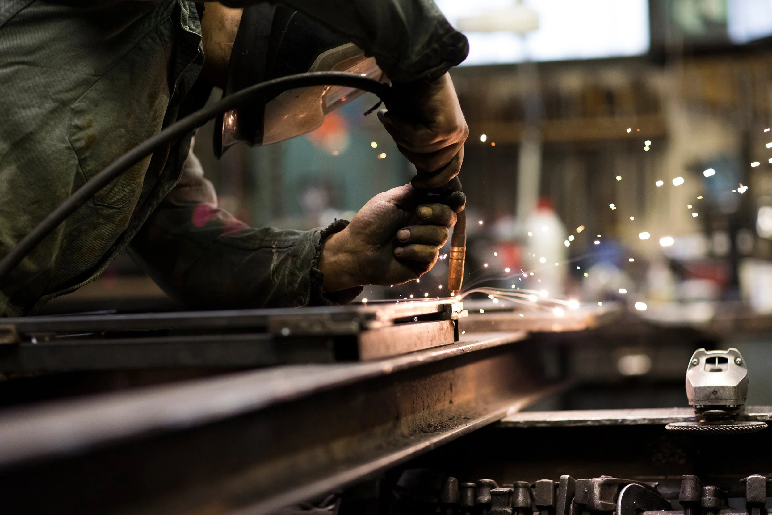 Ein Handwerker schweißt Metallteile, dabei sprühen Funken in einer Werkstatt.