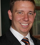 Close-up of a smiling young man with short hair in a suit and striped tie