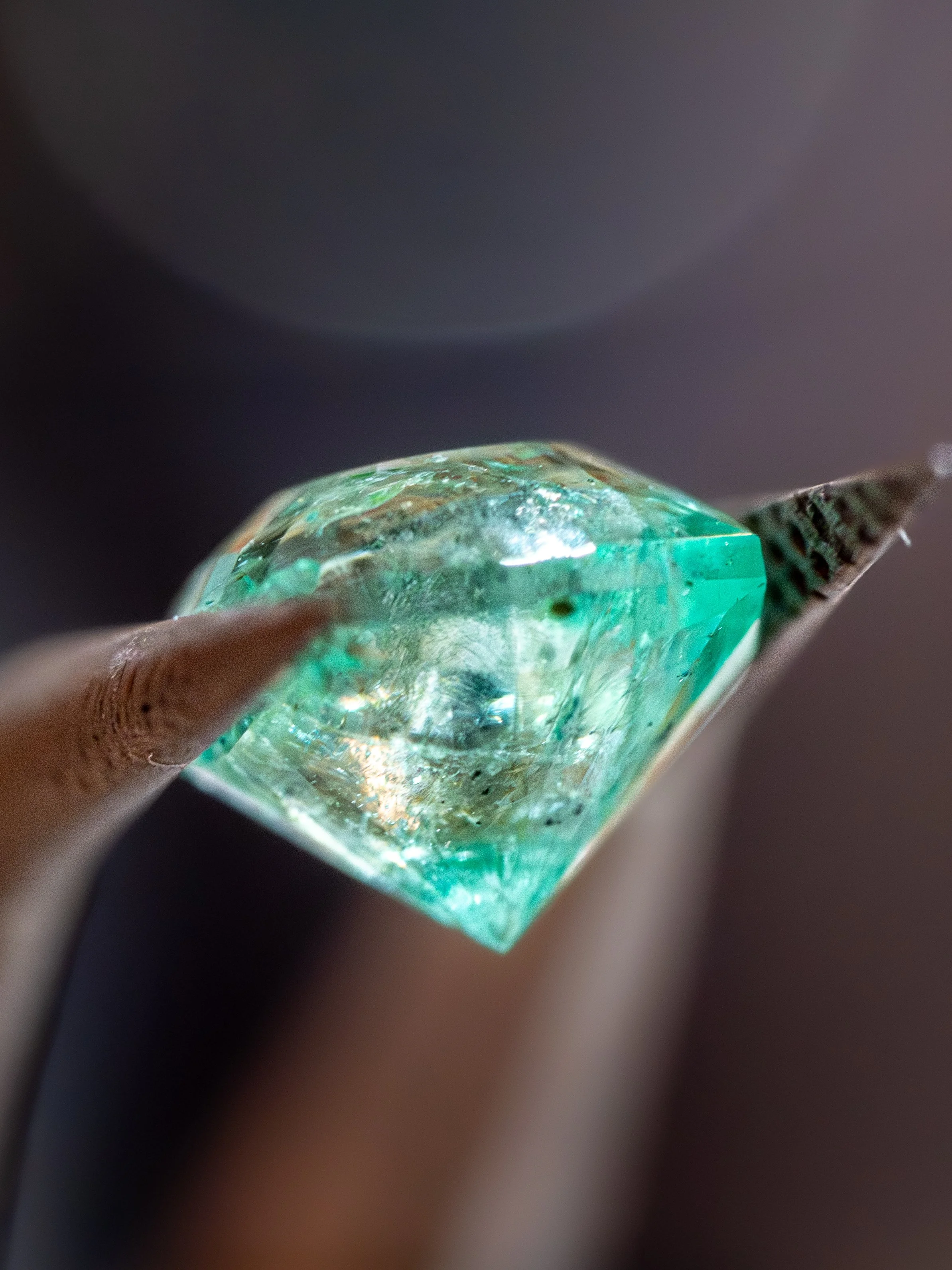 Close-up of a person's hand holding a small, transparent, rectangular glass object with a greenish hue, against a dark background.