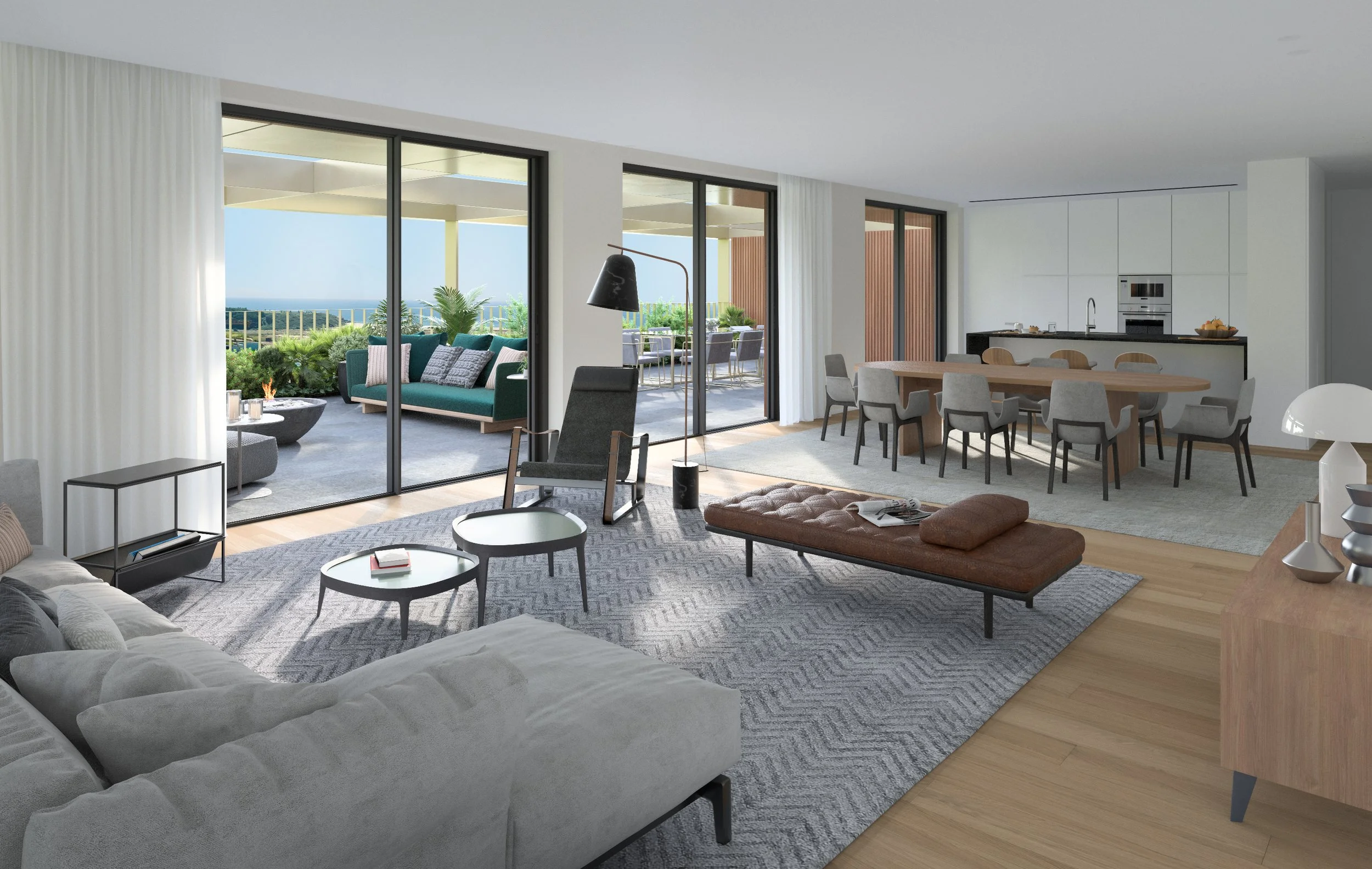 Modern living room with large sliding glass doors leading to balcony with outdoor seating. Inside, there's a white sectional sofa, a gray armchair with a black floor lamp, a beige tufted bench, and round coffee tables on a patterned rug. To the right, an open kitchen with a dining table and multiple chairs is visible, with white cabinets and built-in appliances. The balcony has a green sofa with pillows, and an outdoor dining area with table and chairs. Views of greenery and the ocean can be seen through the glass doors.