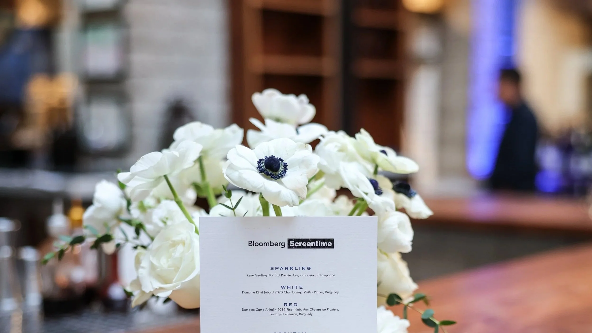 Close-up of a bouquet of white anemone flowers placed on a table with a menu card in front of it at a formal event or restaurant.