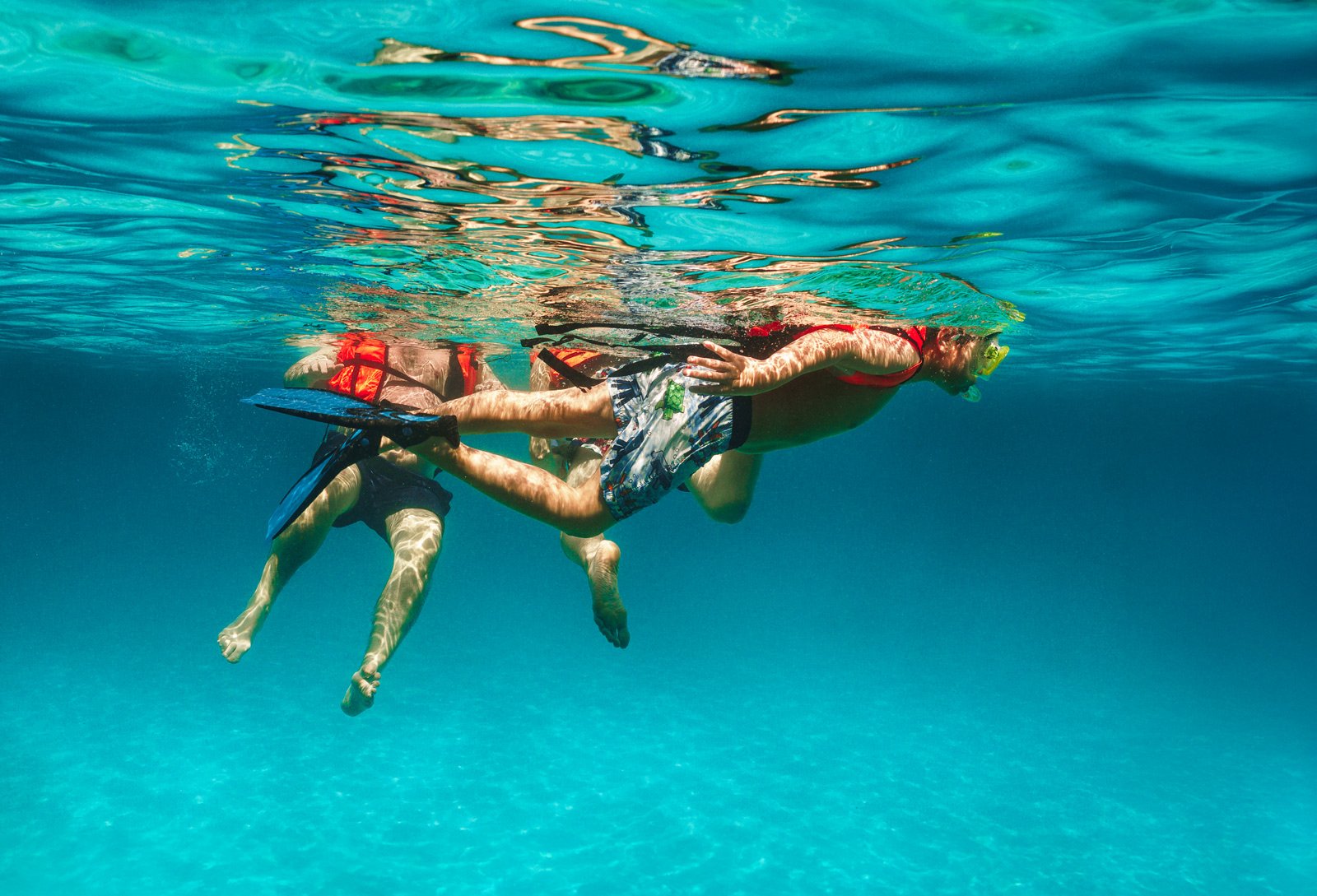 Two children swimming underwater in a pool, wearing swim gear and snorkels.