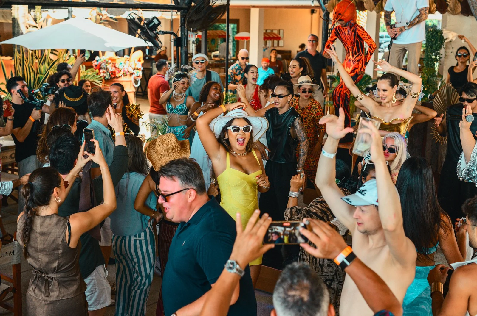 Group of people dancing and enjoying a celebration, with colorful attire and accessories, in a lively outdoor setting.