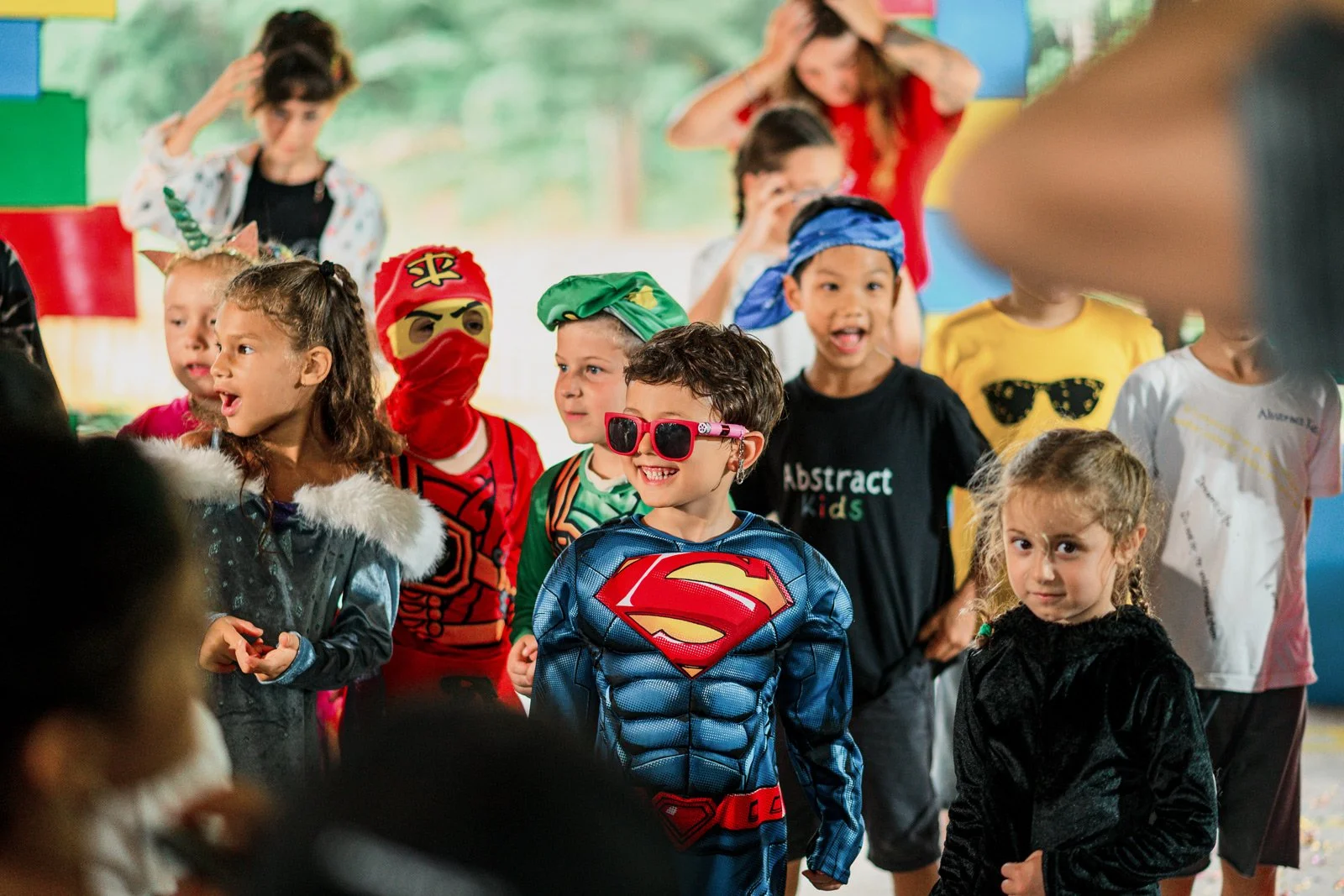 Children dressed in costumes at a party, including Superman, ninja, pirate, and other characters.