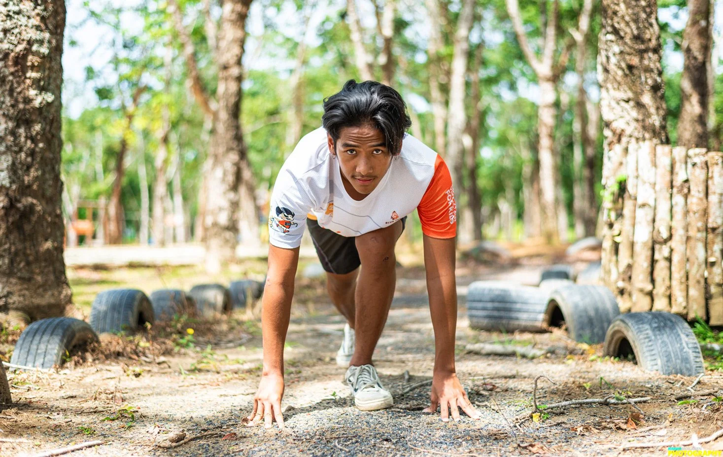 Young man in athletic clothing preparing to start a race on a forest trail, with tires lining the path.