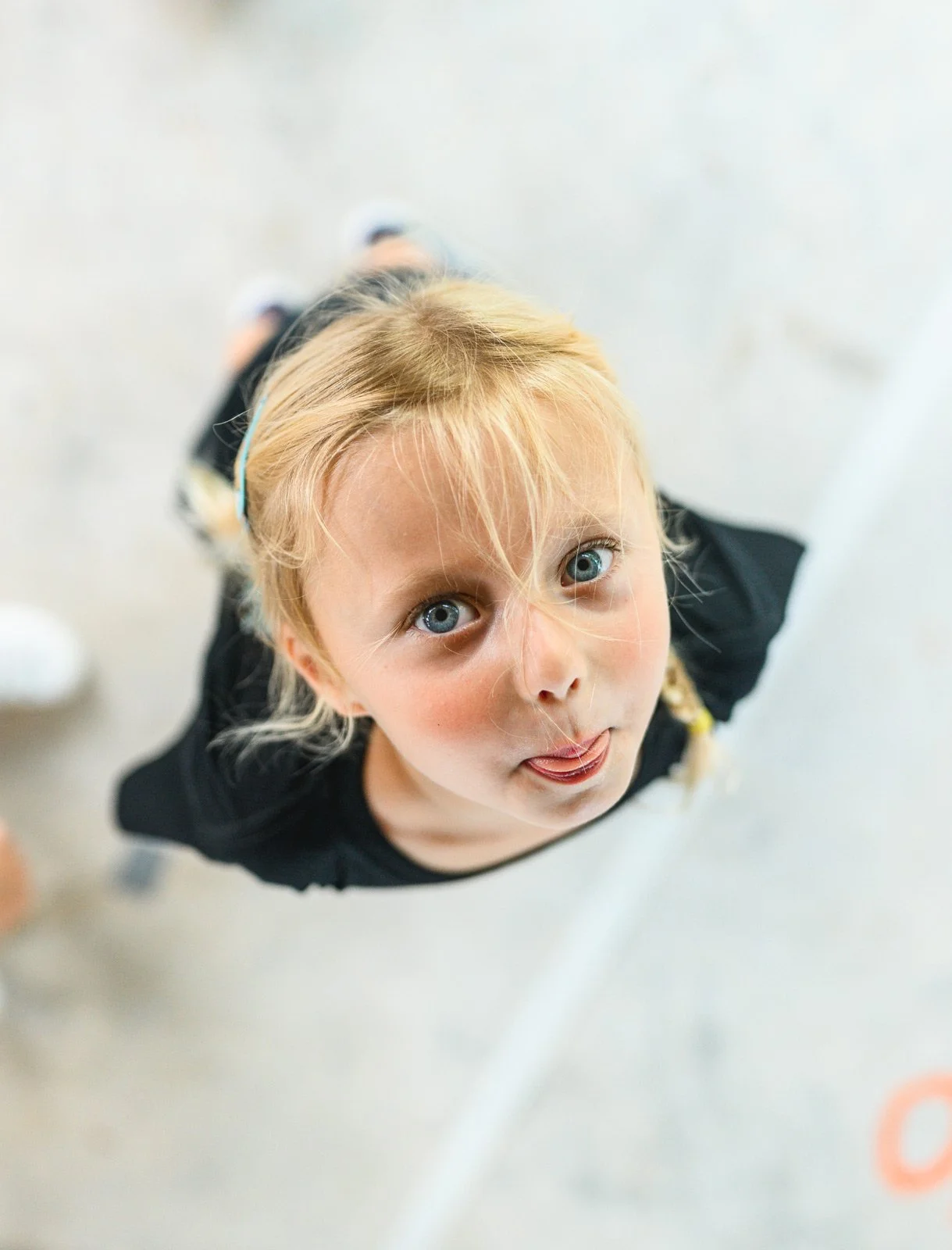 A young girl with blonde hair and blue eyes looking up at the camera and sticking out her tongue.