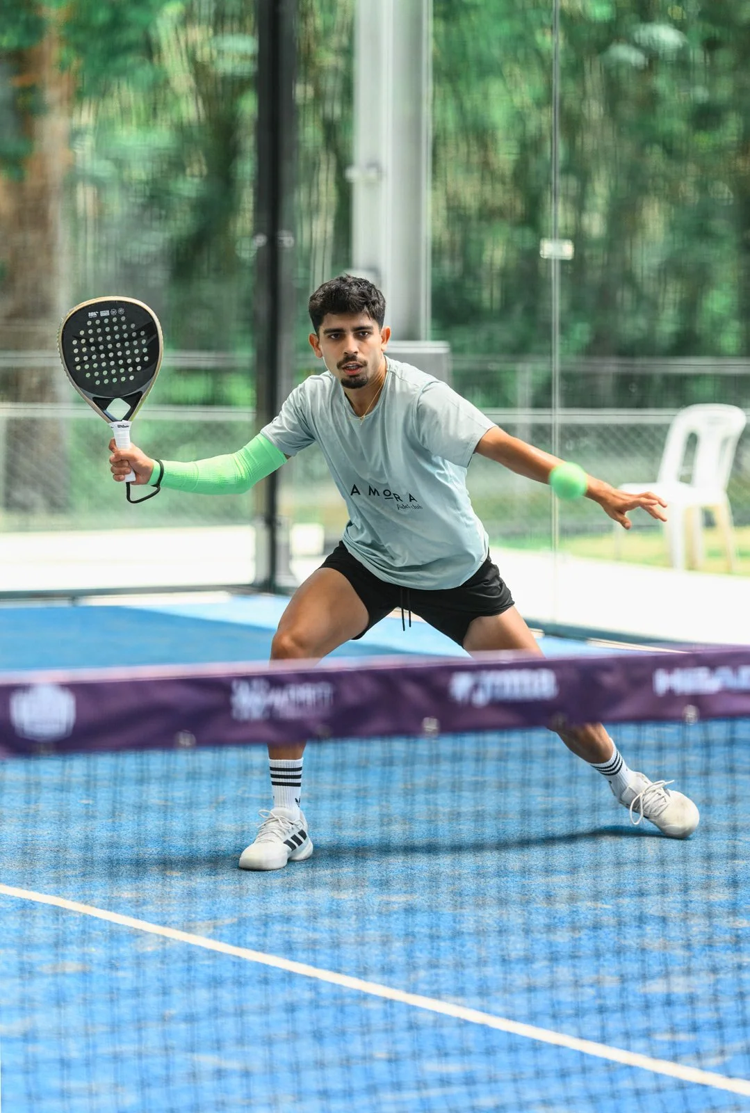 A young man playing padel tennis on an indoor court, holding a racket, dressed in athletic clothes, with a focused expression.