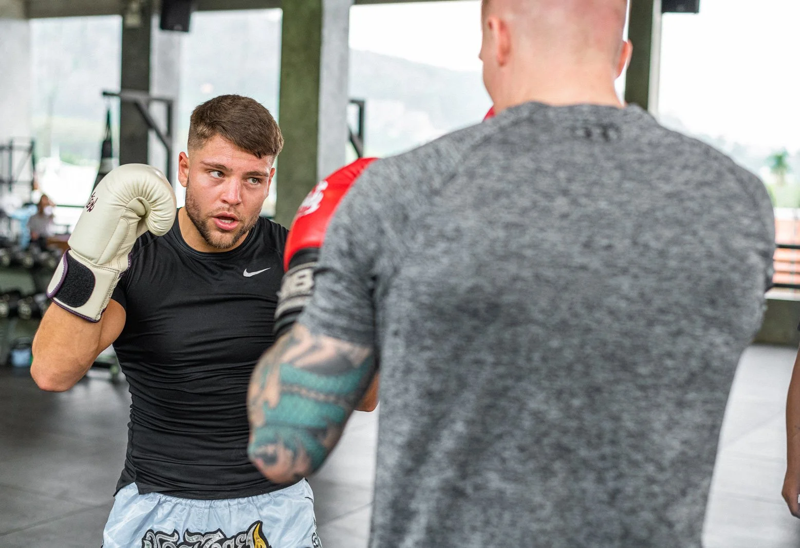 A boxer practicing punches in a gym with a trainer, who is wearing gloves and a gray t-shirt, watching attentively.