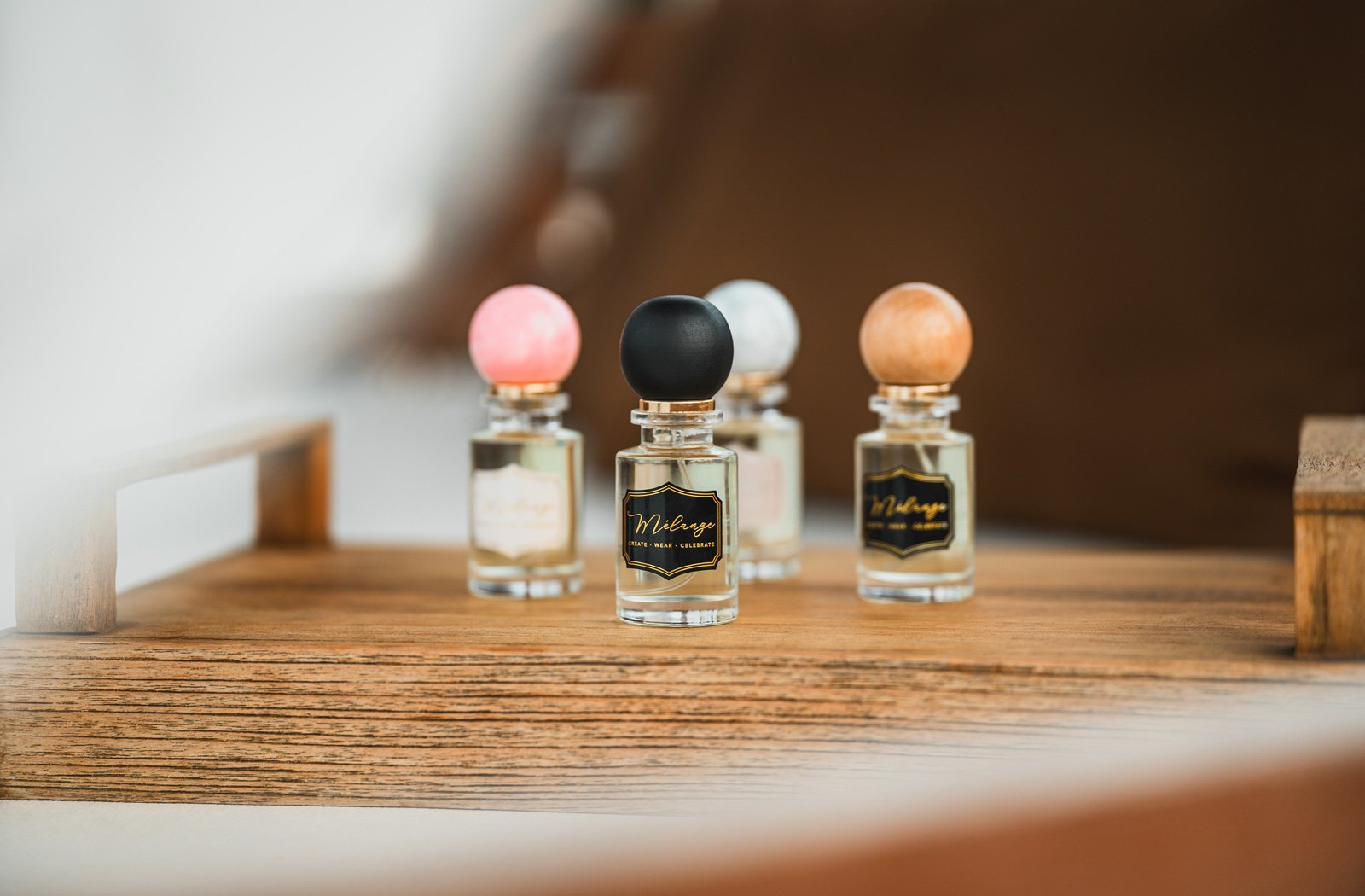 Four small glass bottles with colorful wooden spheres on top, placed on a wooden surface, with a blurred background.
