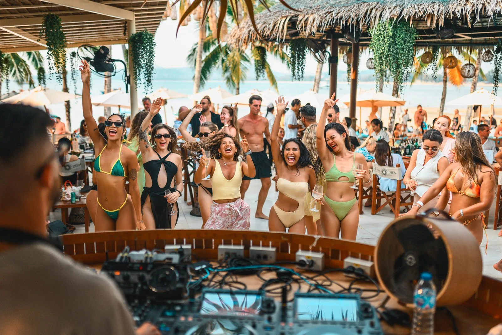 People dancing and enjoying music at a beach bar with palm trees and ocean in the background