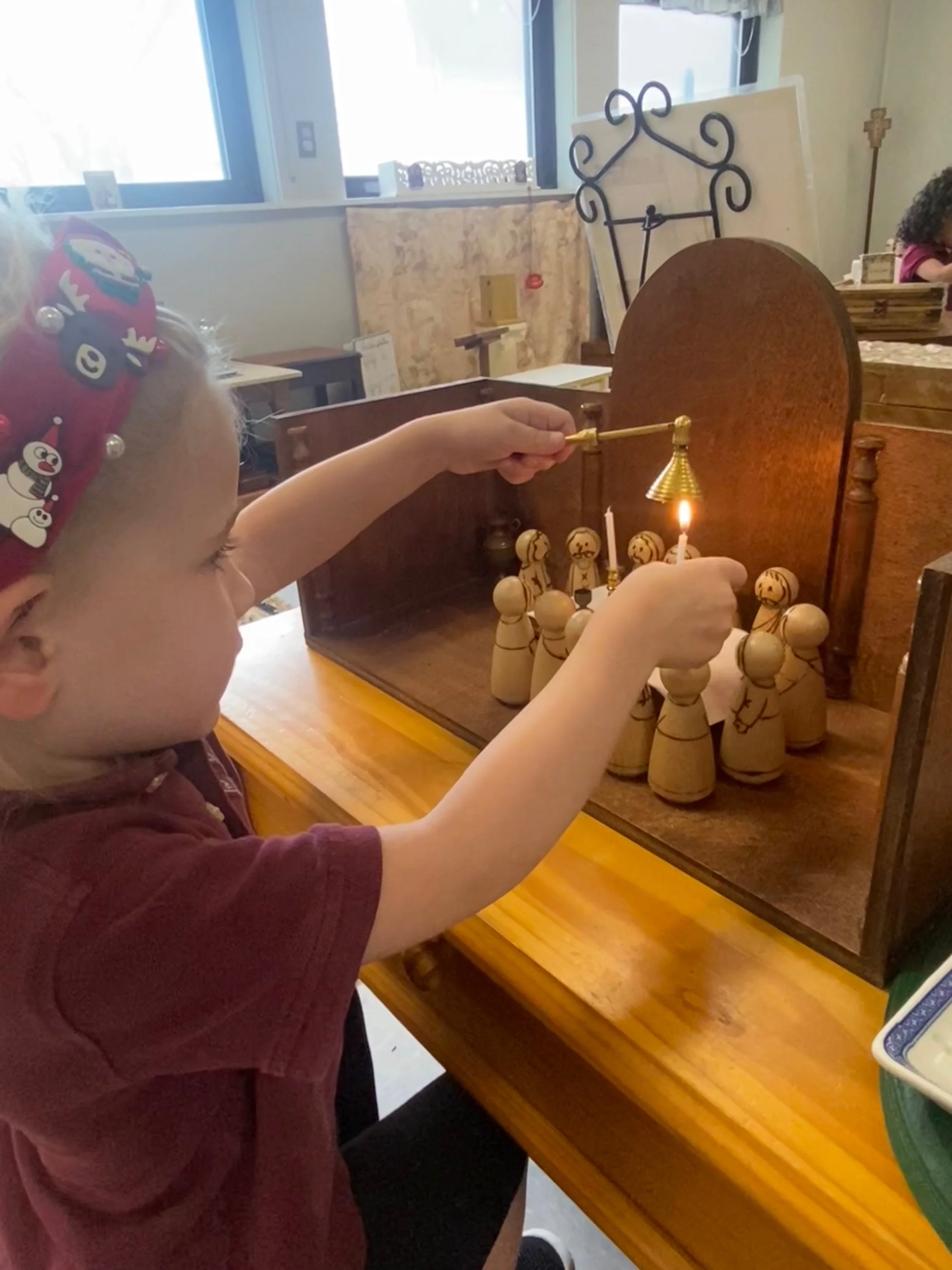 Child wearing a Christmas-themed headband playing a game of chess with a candle and decorated chess pieces on a wooden table.