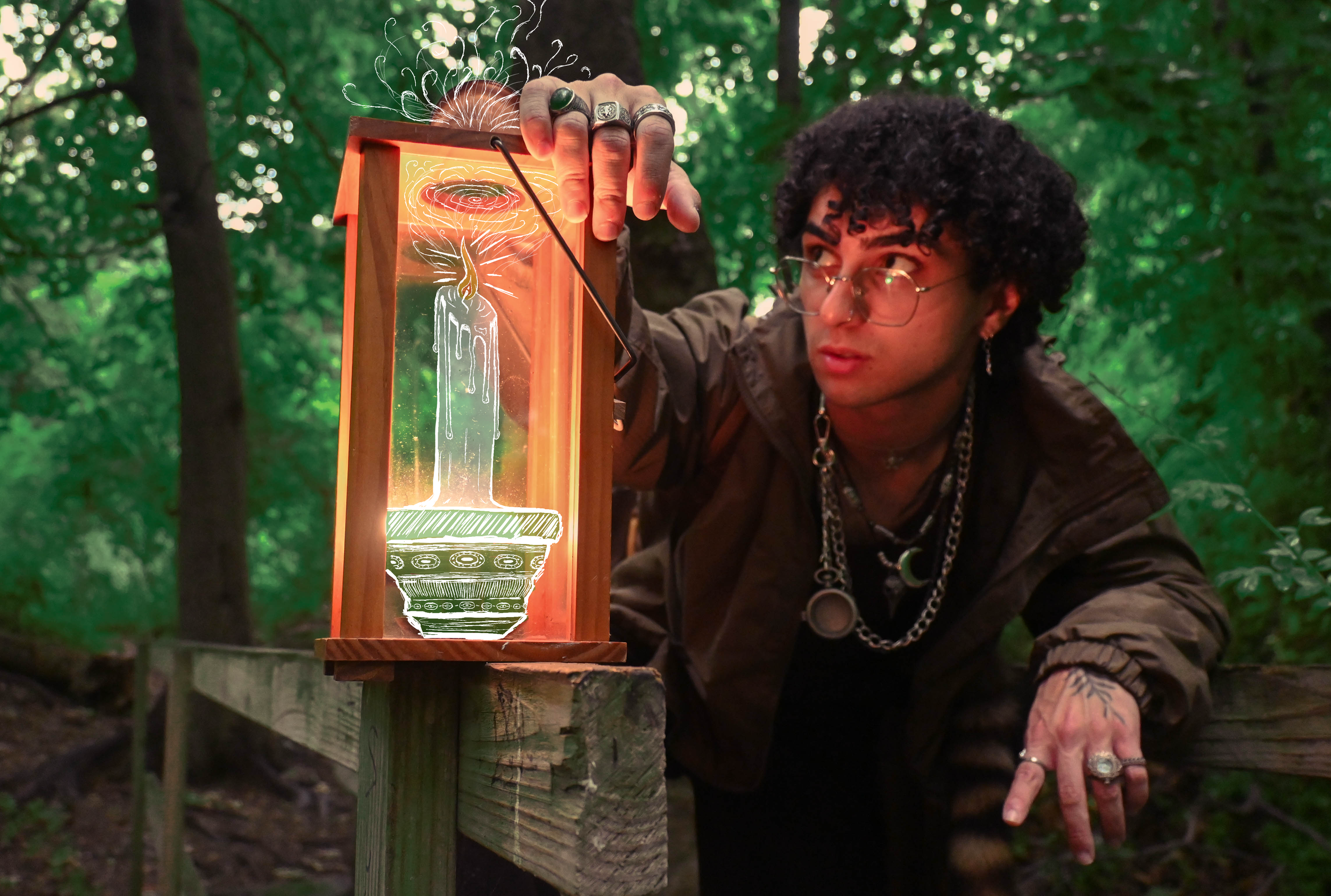 Person with curly hair and glasses, wearing jewelry, adjusting a glass light fixture with a drawn candle illustration, in a forest setting.
