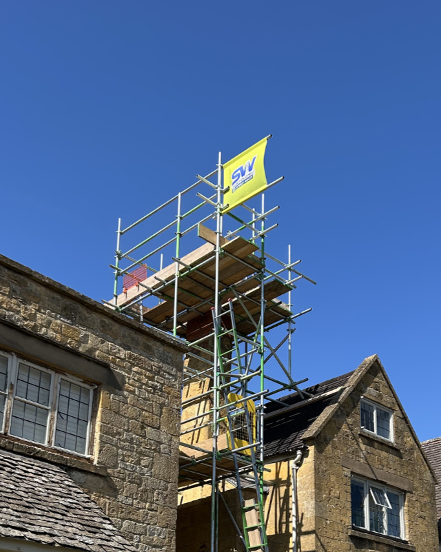 Scaffolding and a flag on top of a stone building under a clear blue sky.