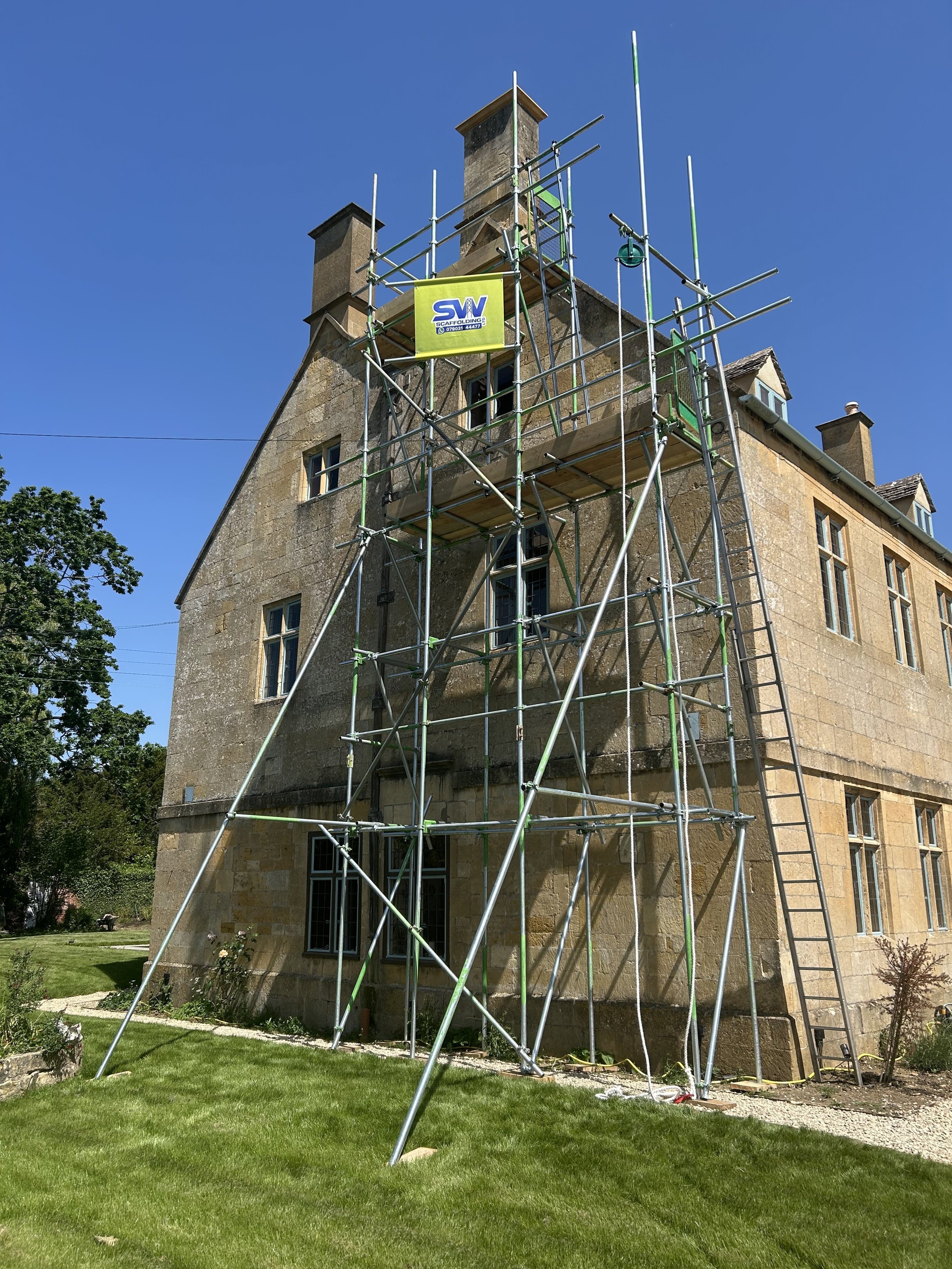 A large stone building under renovation with scaffolding surrounding it, set against a bright blue sky.
