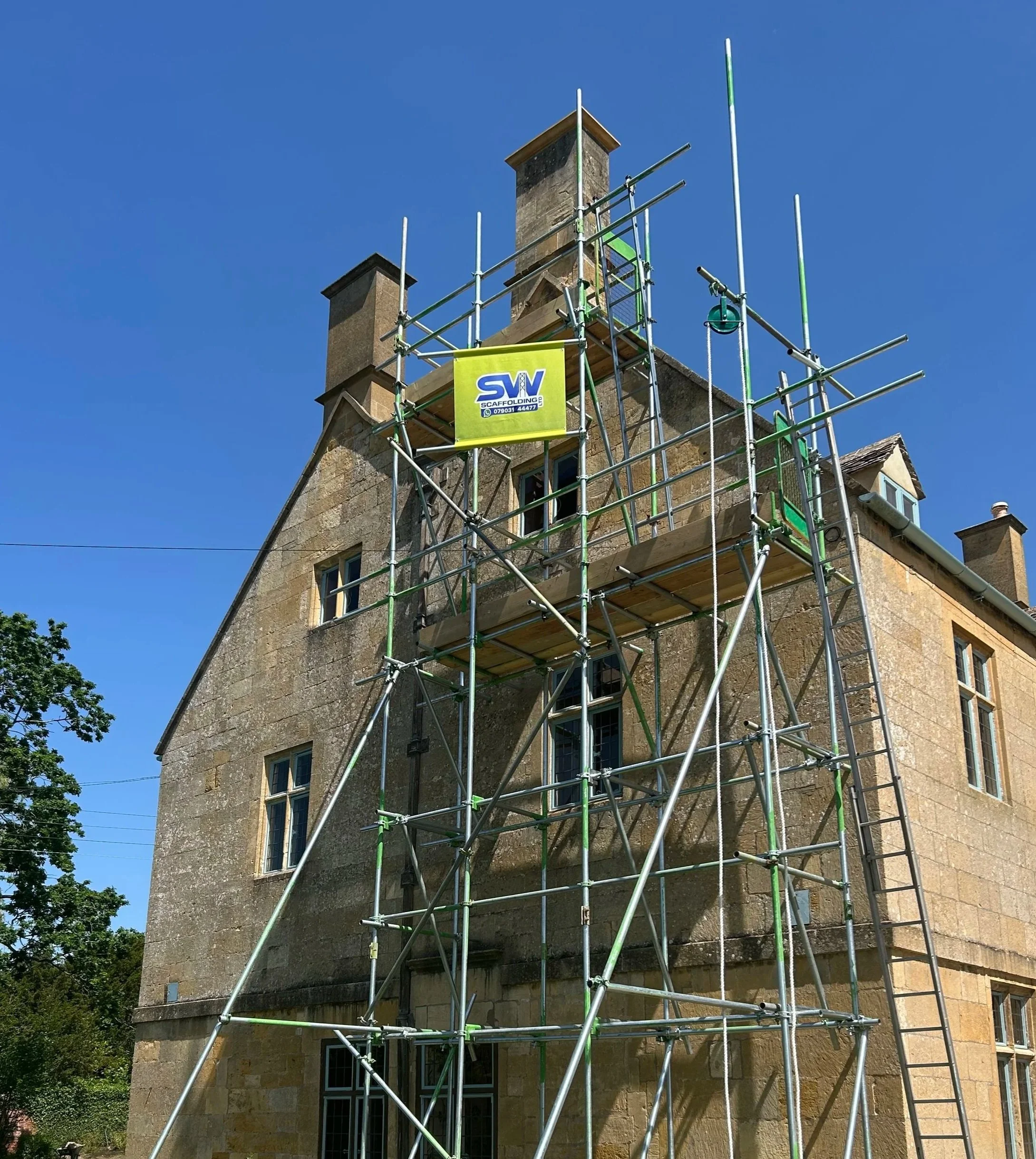 Construction scaffolding surrounds an old stone building with multiple windows and two chimneys.  Scaffolding service from SW Scaffolding.