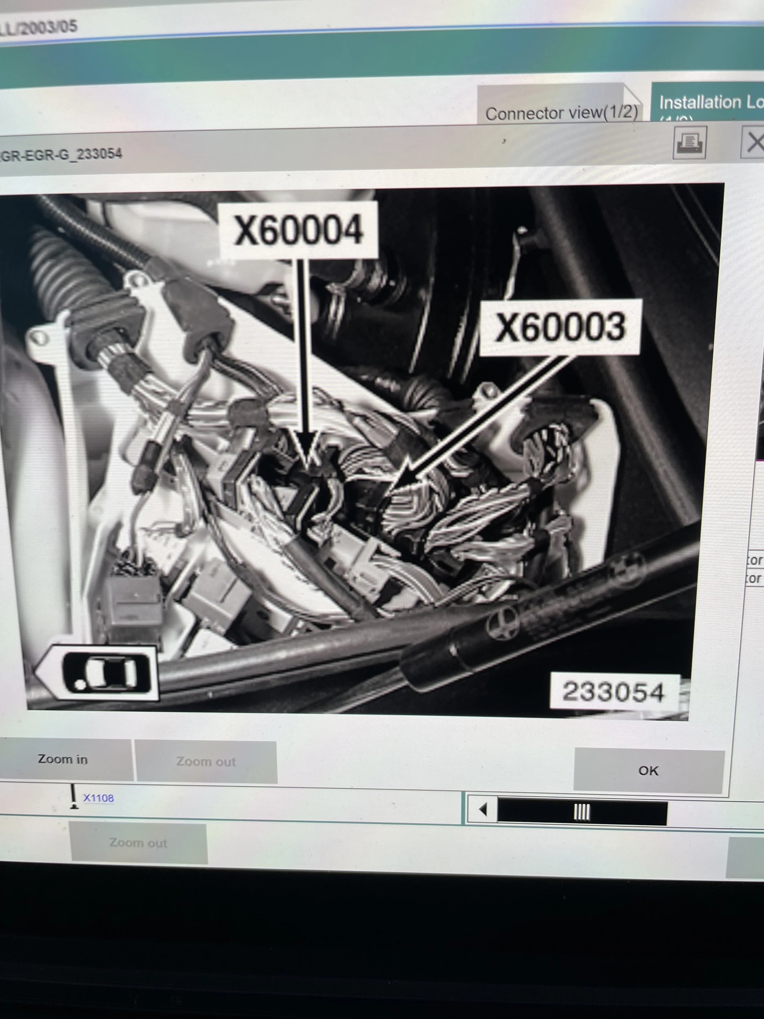 Close-up photograph of an automotive engine with labels indicating parts X6004 and X6003, showing various hoses, wires, and mechanical components.