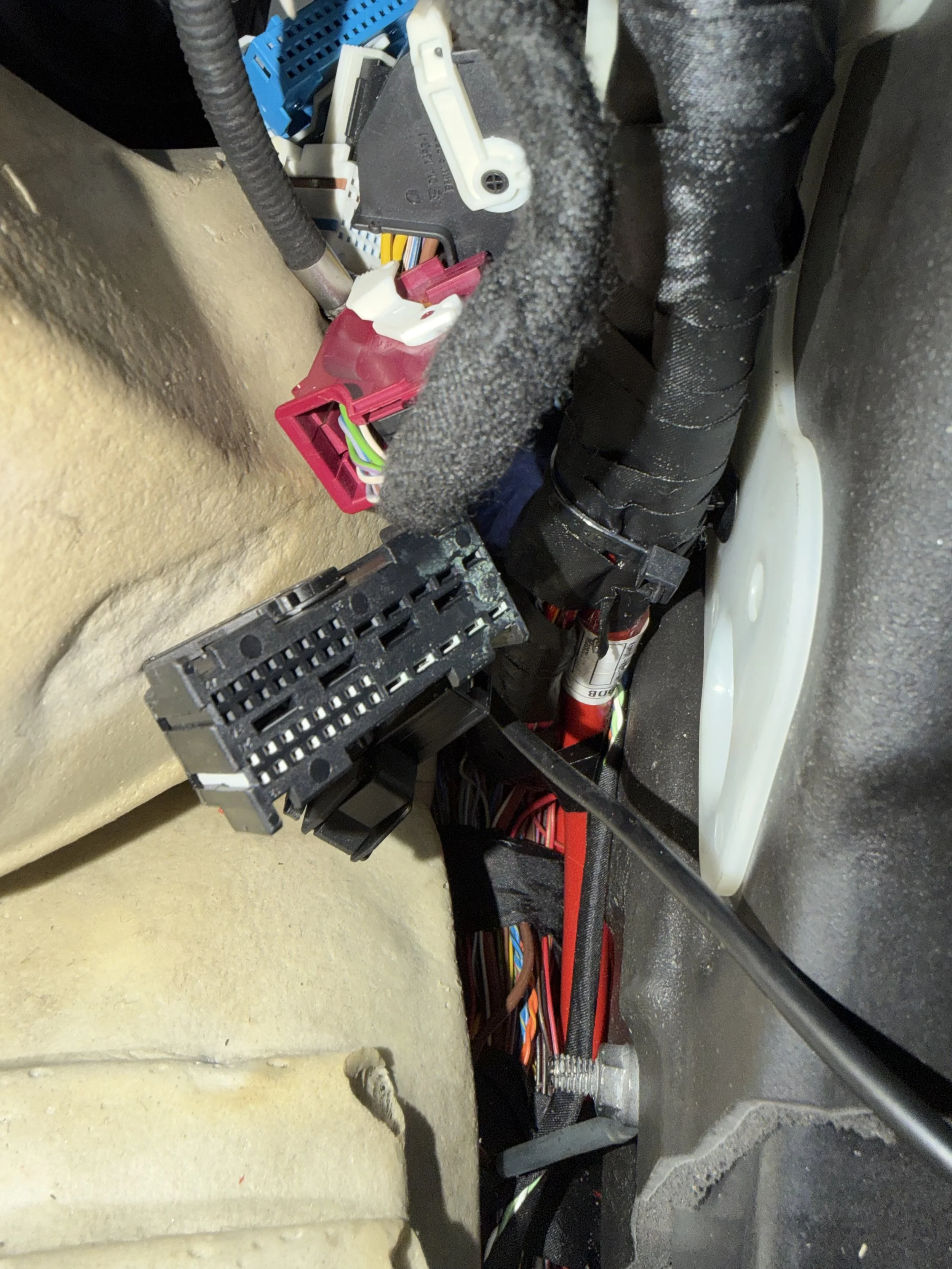 Close-up of a bundle of multicolored wires and electronic components on a black surface, with some protective foam padding and a partial view of a plastic container.