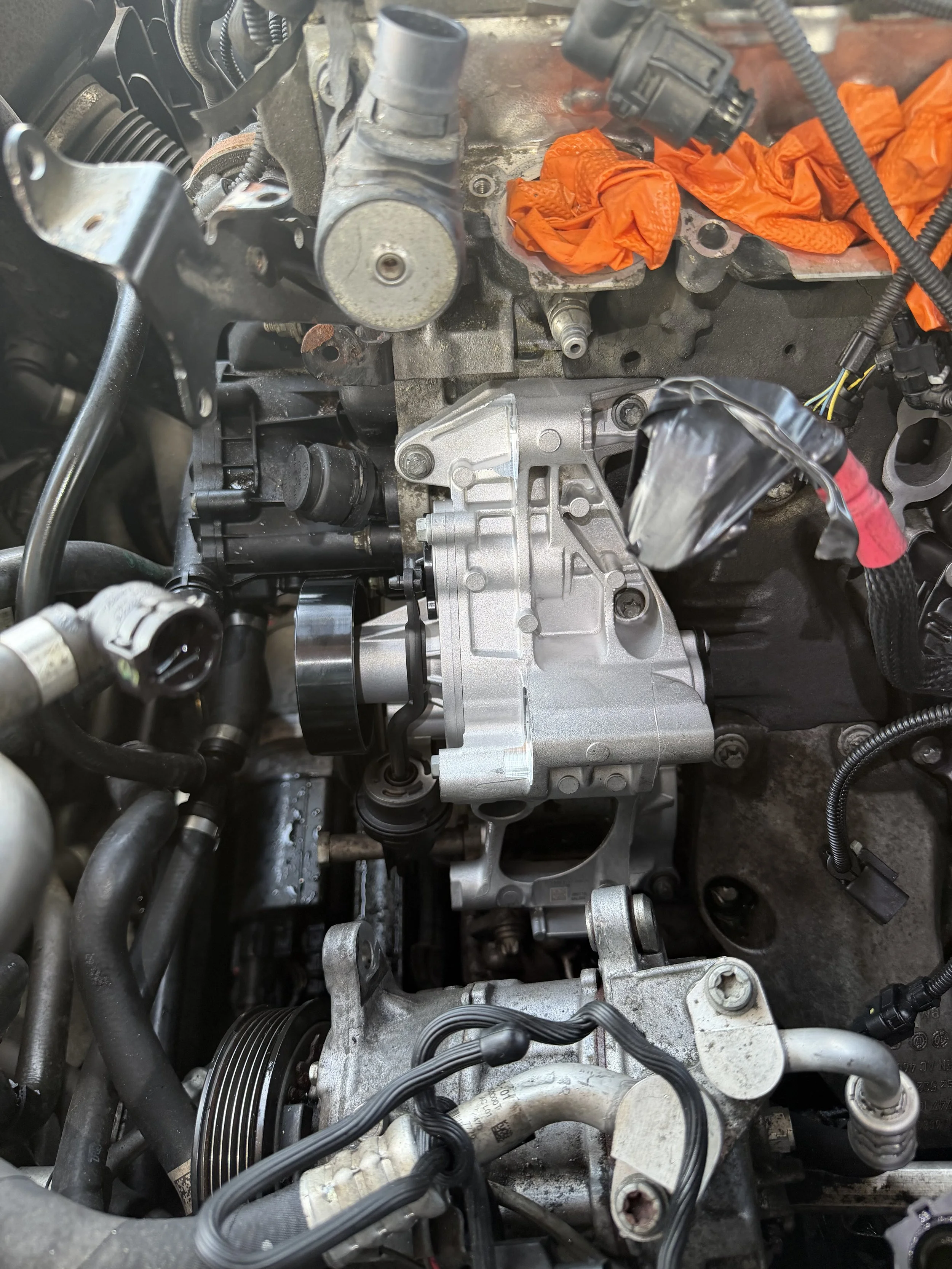 Engine compartment with various components, pipes, wires, and orange cloths or rags inside the engine bay.