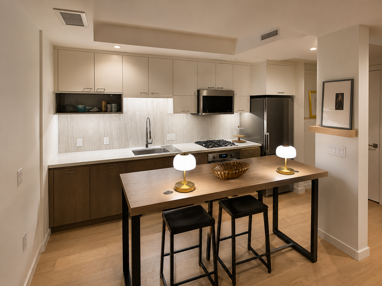 Modern kitchen with white upper cabinets, dark lower cabinets, and a wooden island with two black stools, featuring a white countertop, a stove, microwave, refrigerator, and decorative lamps on the island.