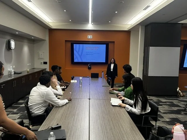 A business team in a conference room participating in a presentation, with a projector screen displaying a slide.