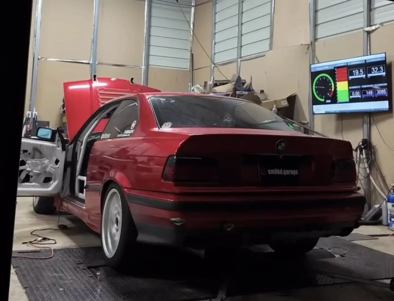 Red race car on a dynamometer with a digital display showing speed, temperature, and other performance metrics.