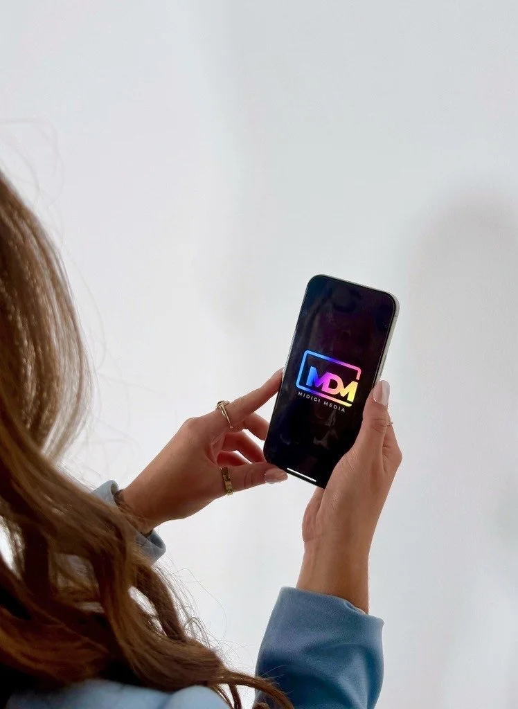Person holding a smartphone displaying the MIDCI Media logo with a white background