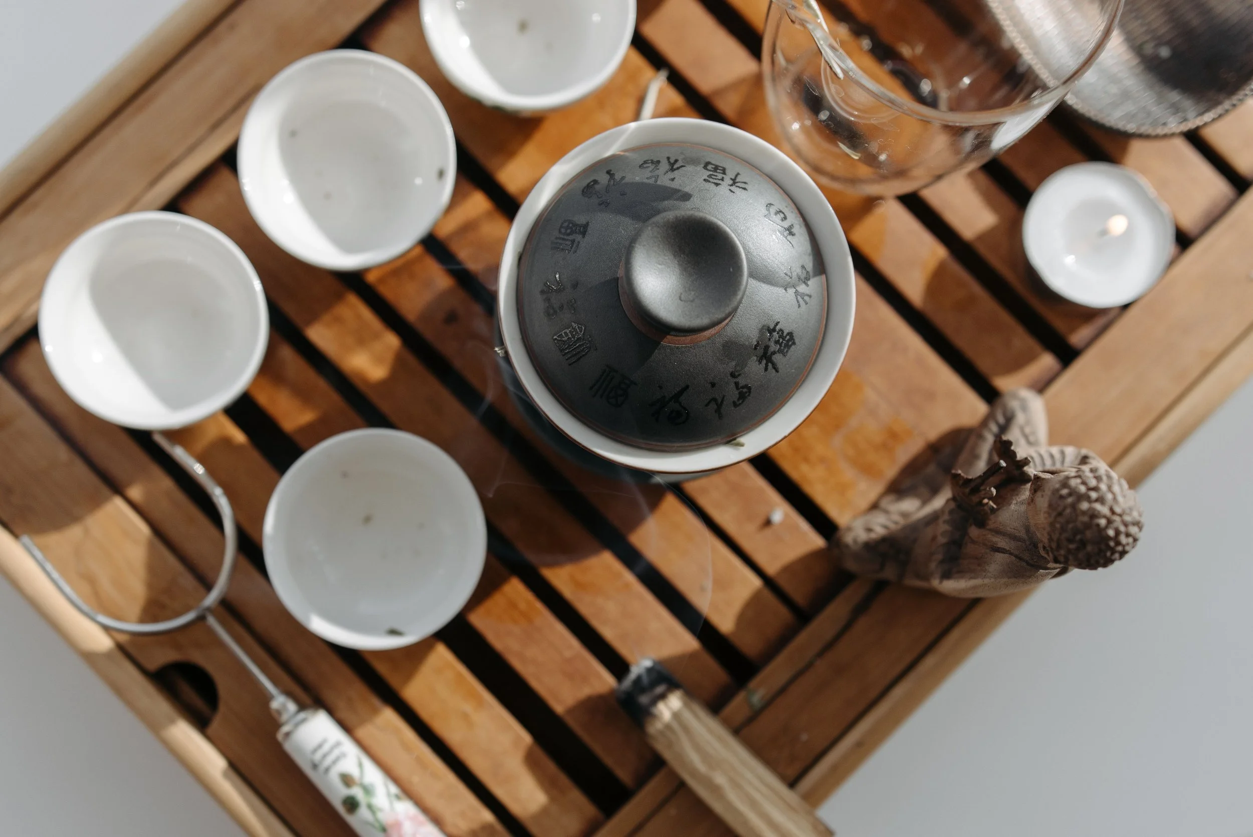 Top view of a wooden tray holding empty white bowls, a glass cup, a small salt shaker, and a black lid with Chinese characters on it.