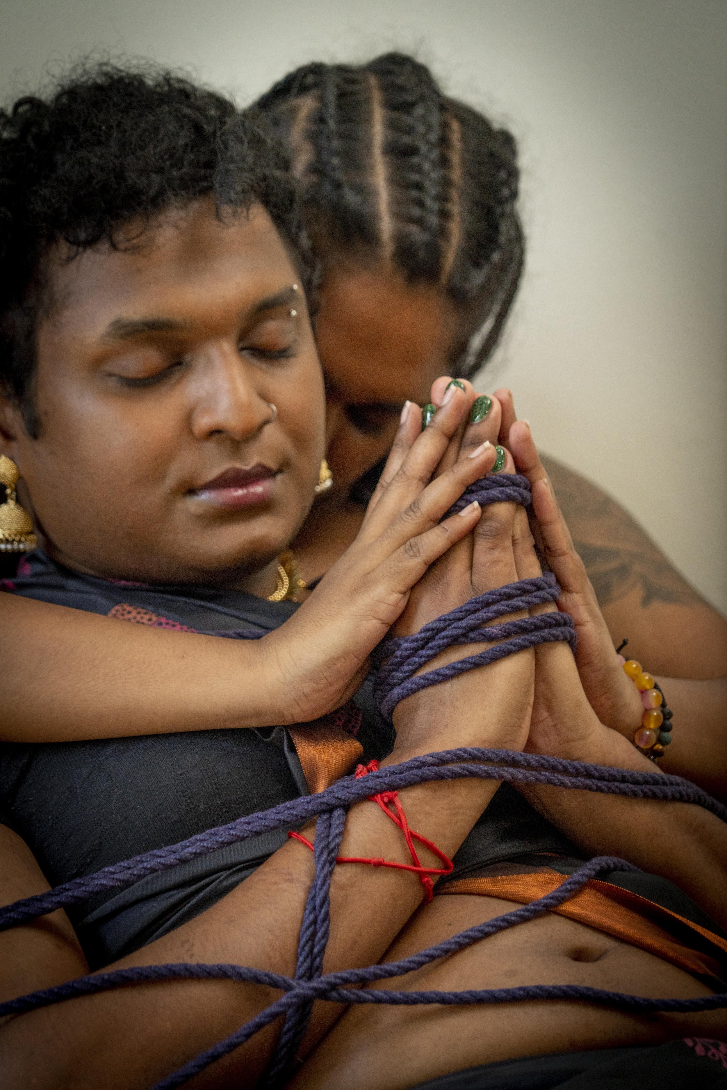 Two women with intertwined purple ropes, practicing meditation with ropes with closed eyes in a peaceful setting.