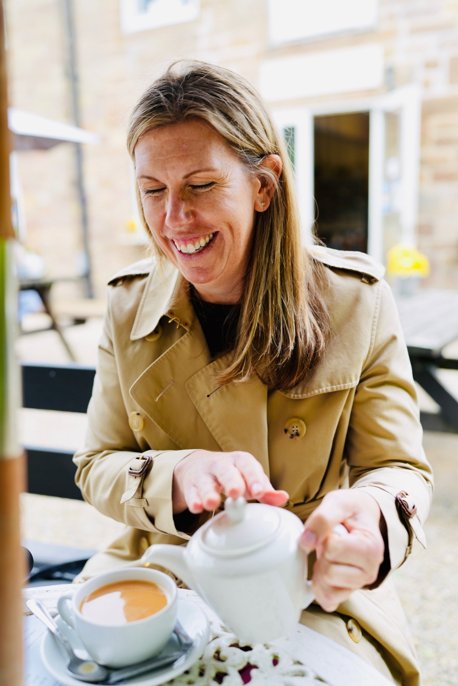A blonde woman, Brooke Van Dam, smiling and looking down pouring a cup of tea.