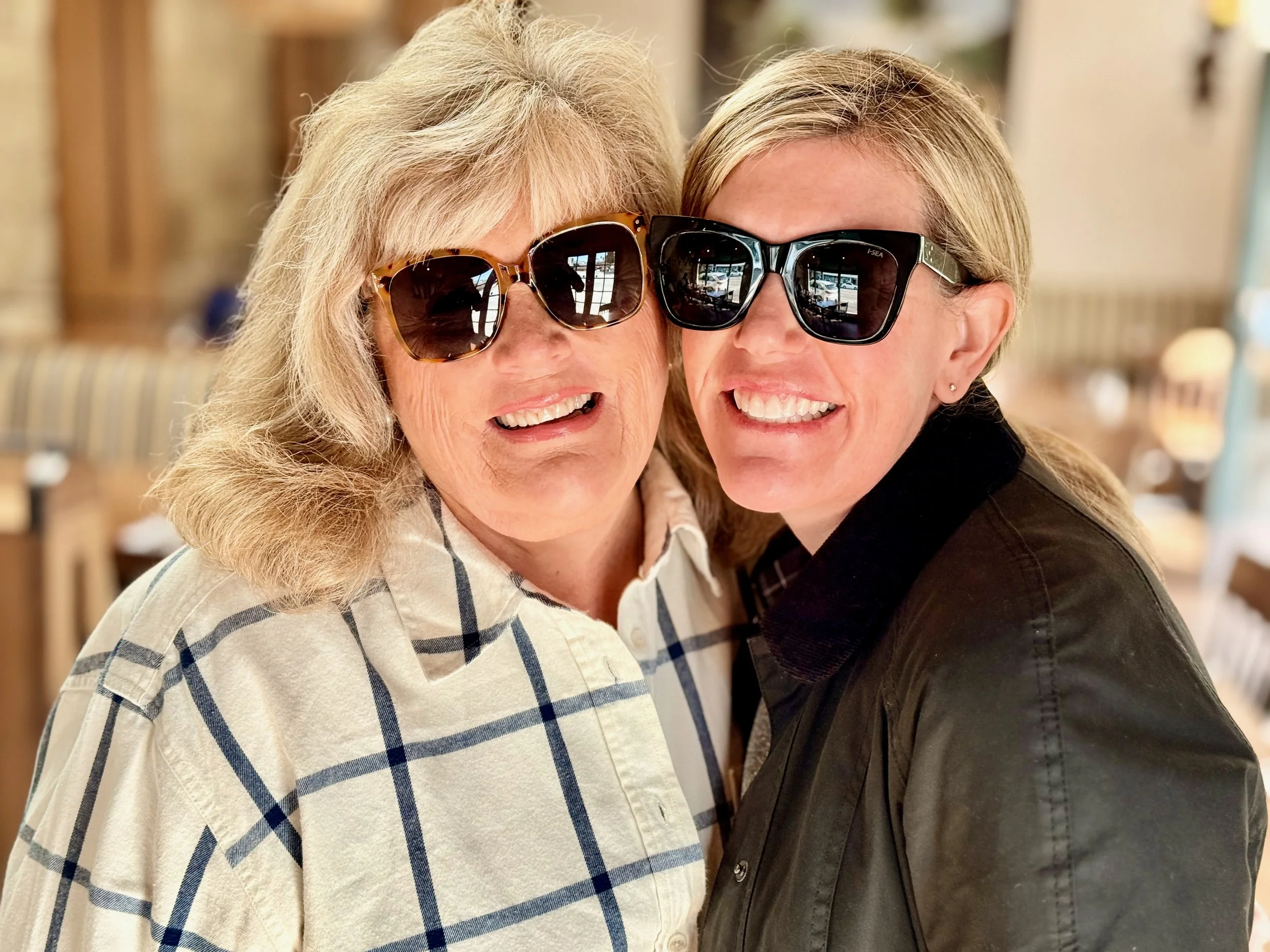 Two women (from right, Brooke Van Dam and her mom) smiling looking into the camera in a bright room wearing sunglasses.