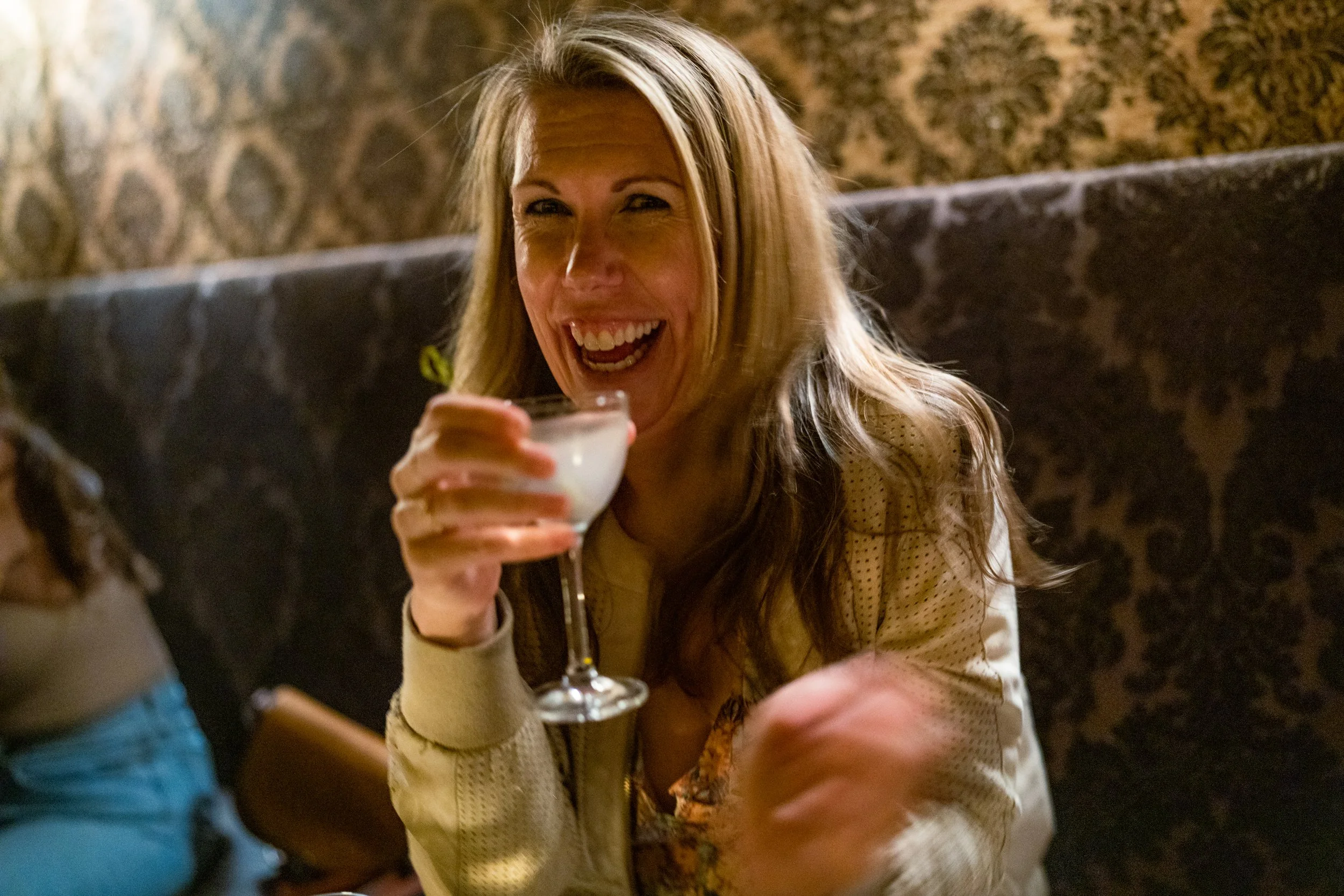 A woman, Brooke Van Dam, smiling and looking into the camera while holding a gin martini at a cocktail bar